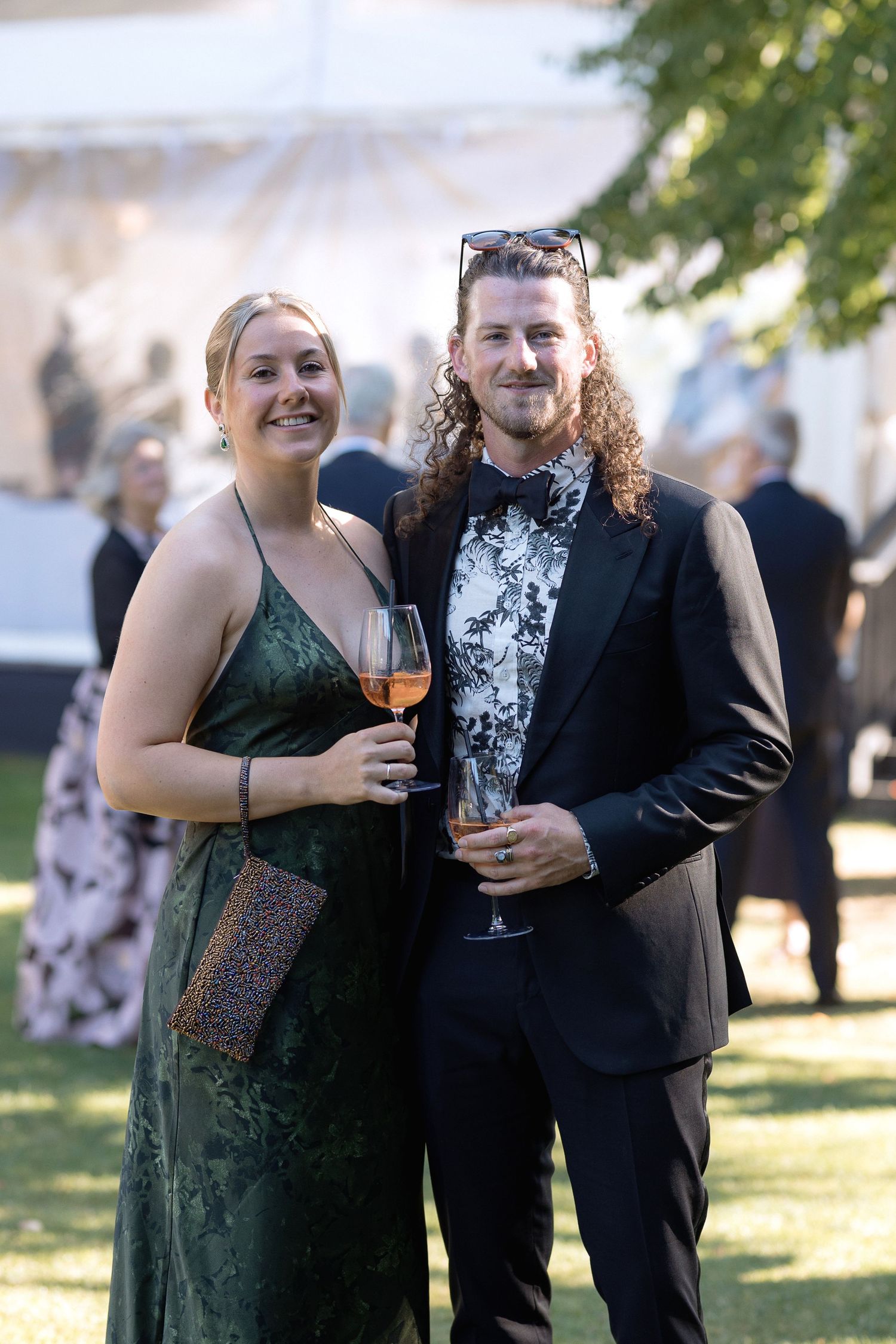 A couple shares a laugh while holding wine glasses at an outdoor event.