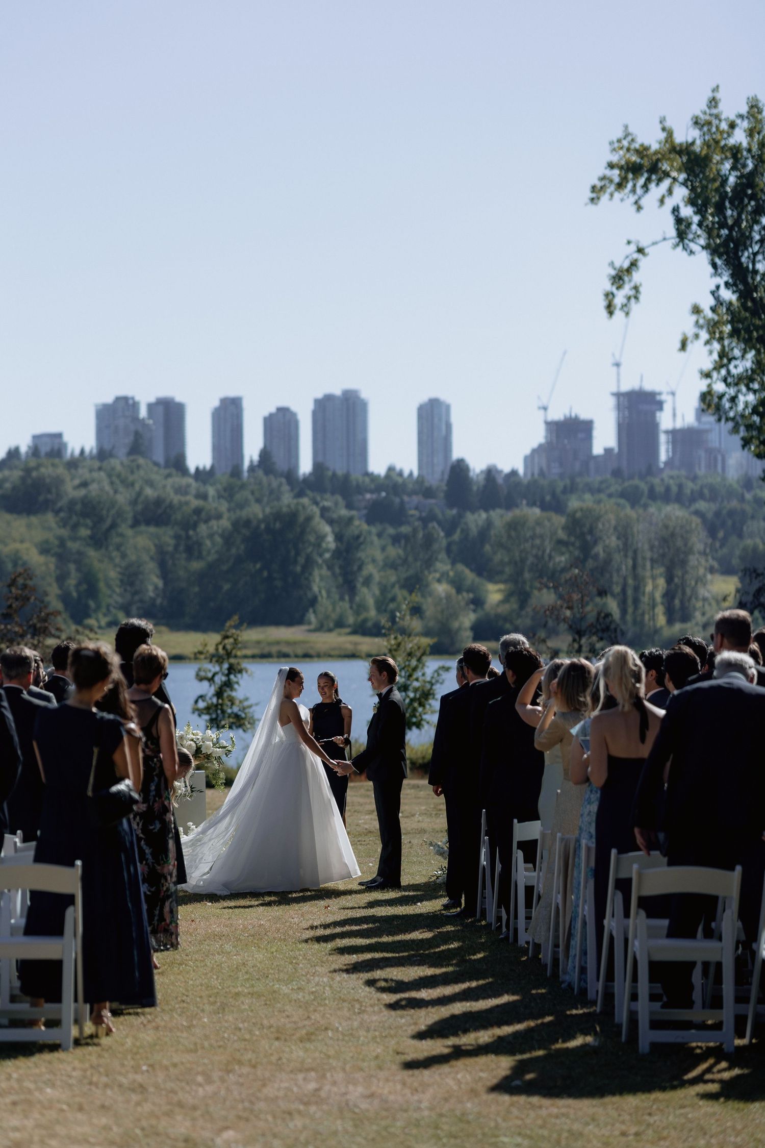 An outdoor wedding ceremony with white chairs and city skyline visible in the background.