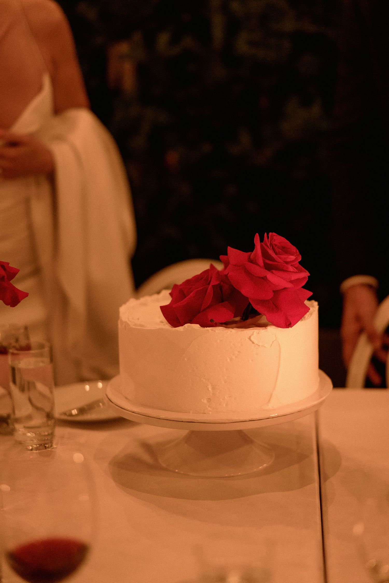 Elegant white wedding cake decorated with red roses on a cake stand.