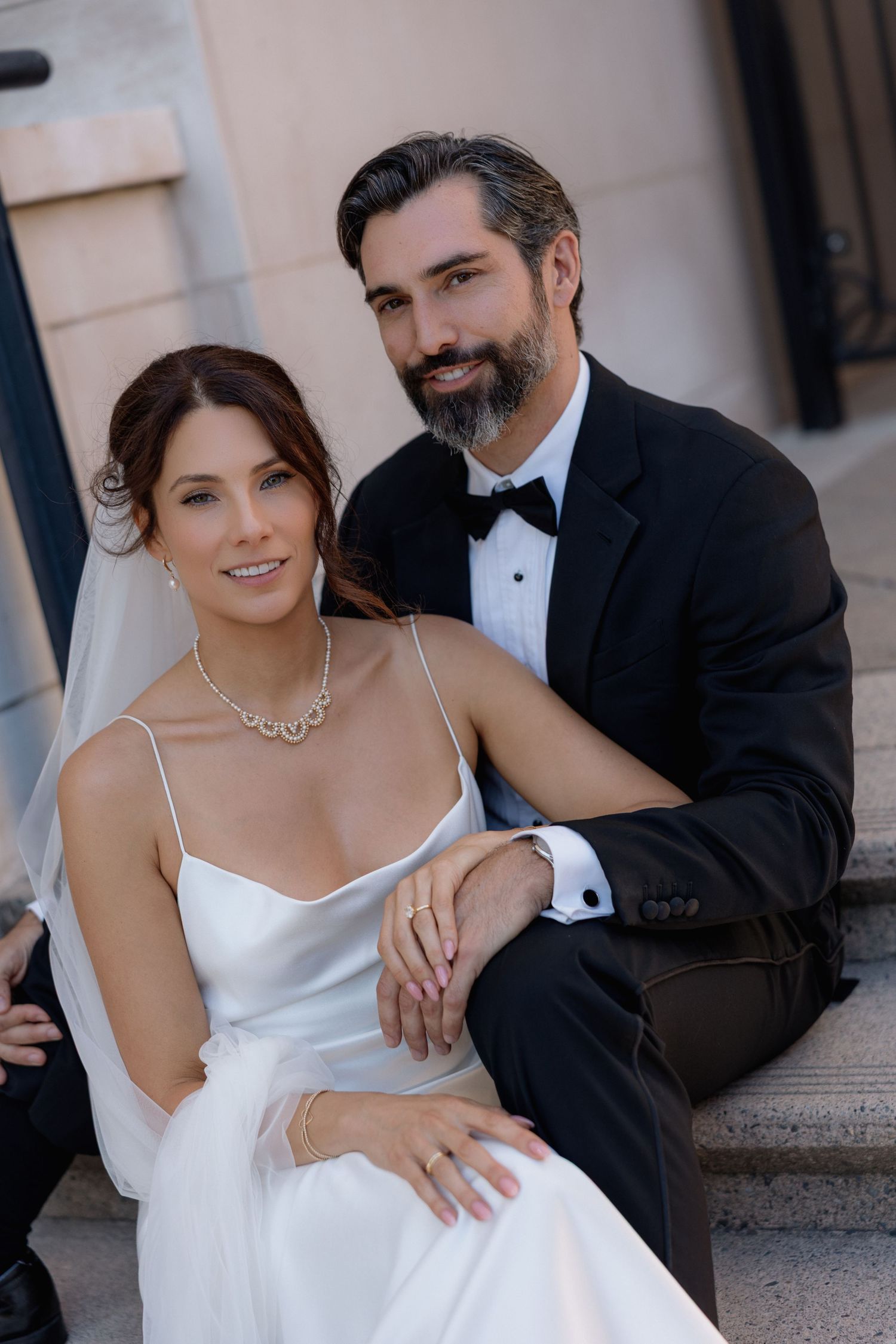 Romantic wedding couple poses intimately on stone steps in formal attire.