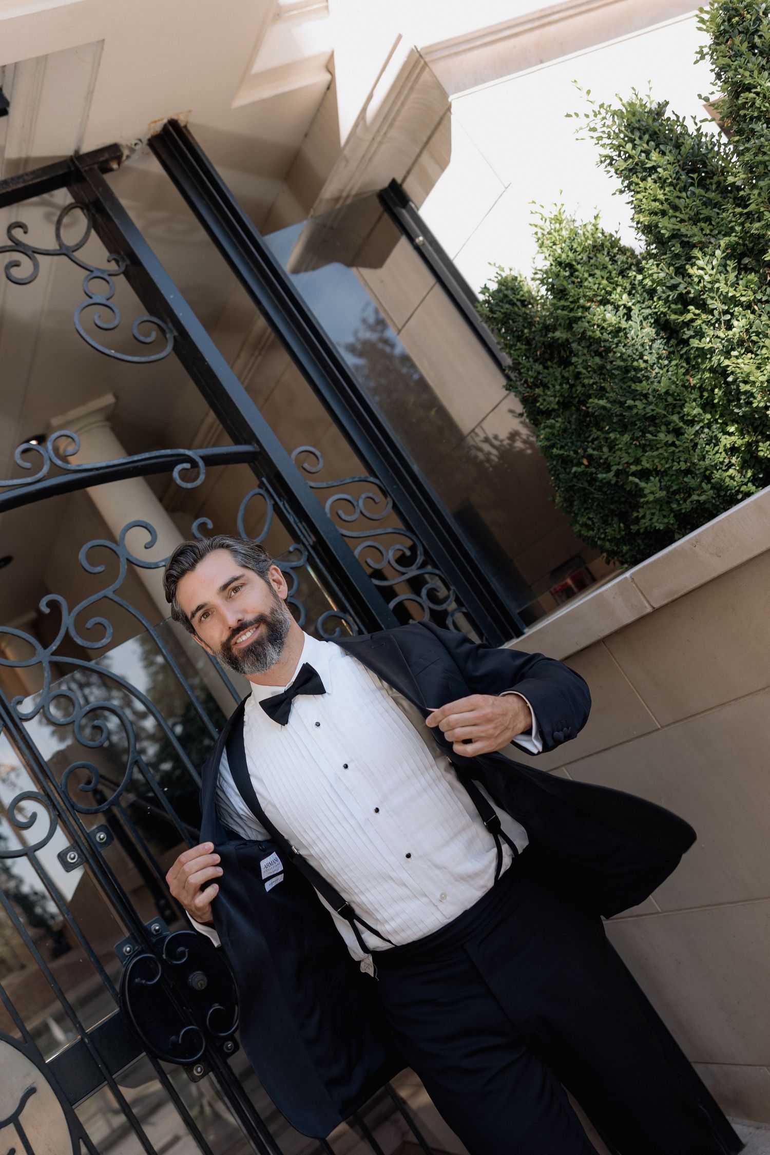 Elegant groom in tuxedo standing by ornate iron gates and columns.