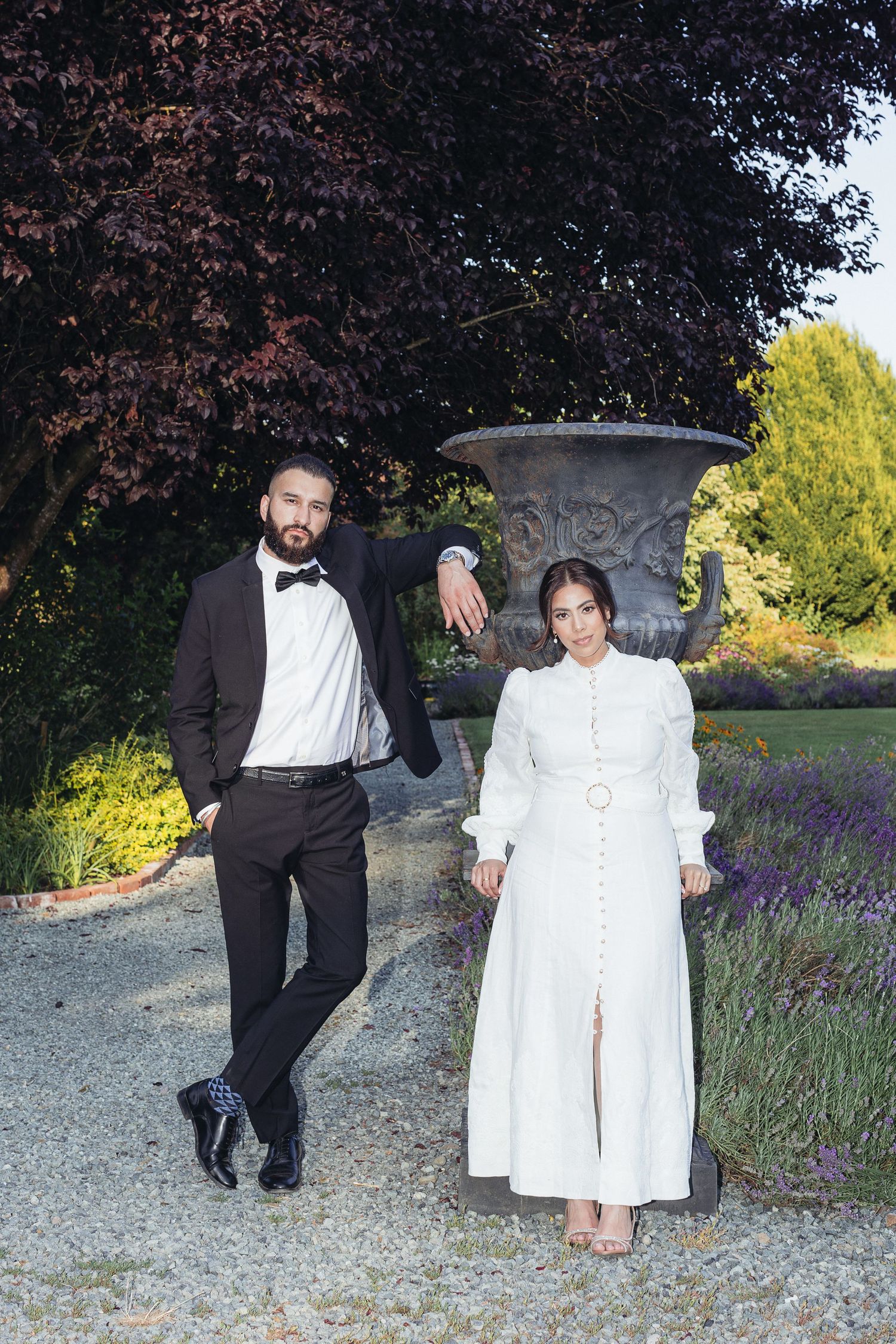 A couple poses playfully in a garden setting with lavender flowers and dark foliage in the background.