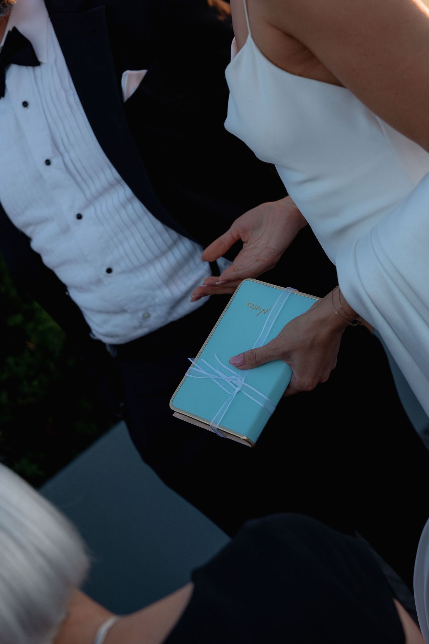 Close-up of hands holding a small turquoise book during wedding ceremony.