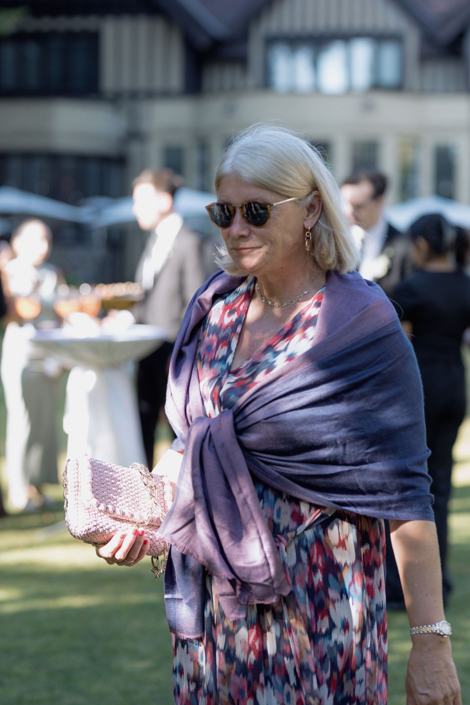 Guest in a purple floral dress with matching shawl enjoys the outdoor wedding festivities.