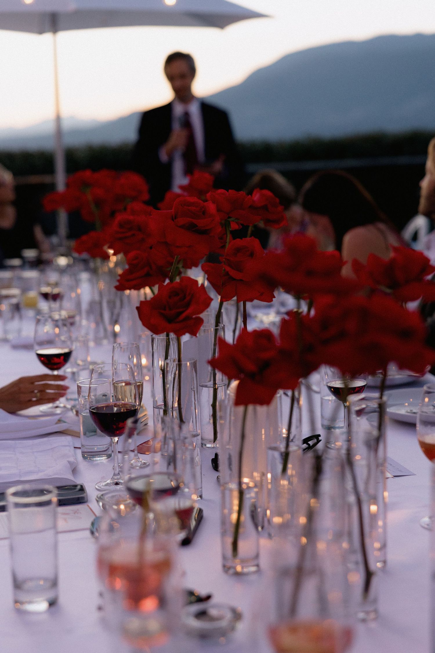 Elegant table setting with red roses in individual vases and wine glasses.