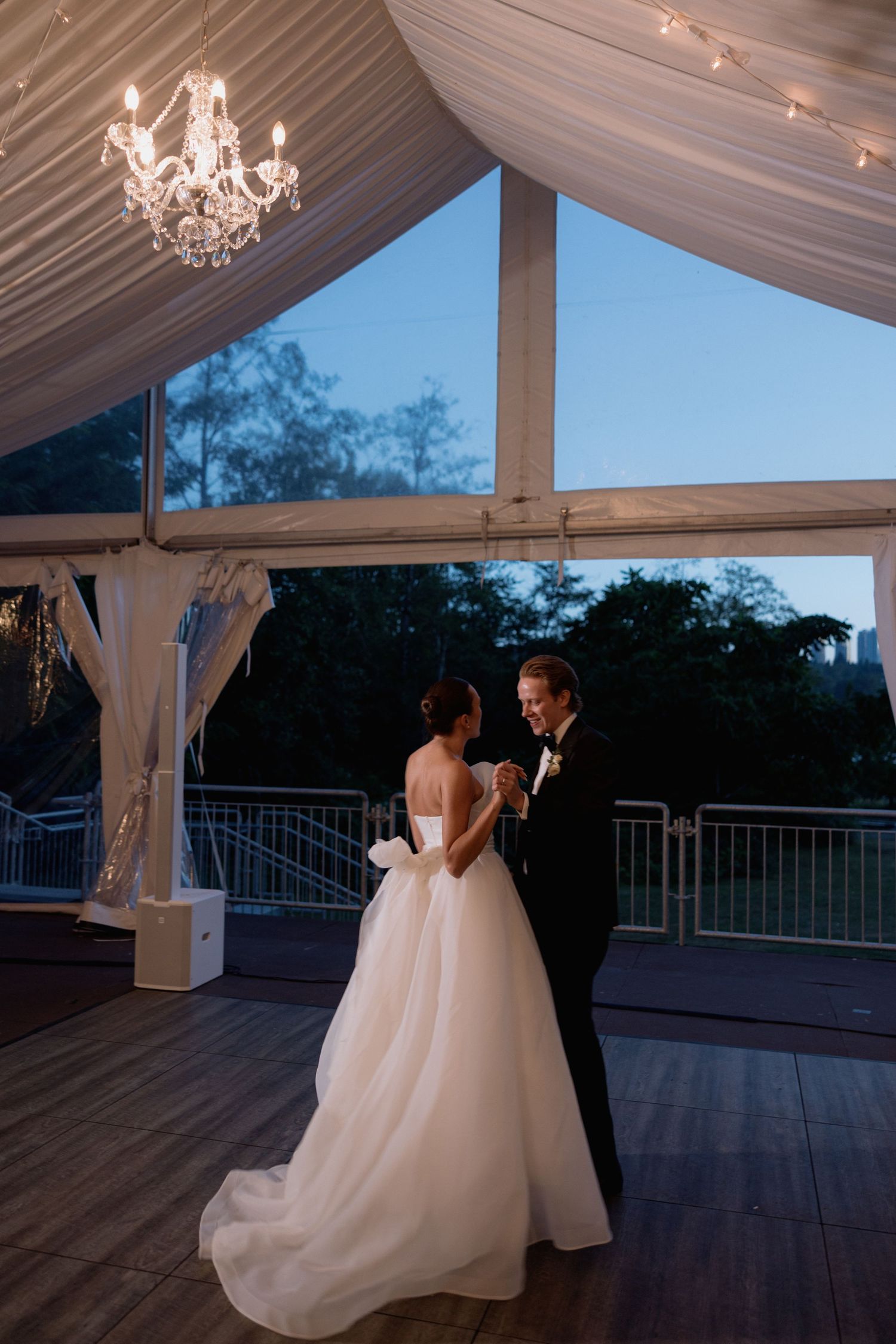 Couple dancing under a draped tent with chandeliers at dusk.