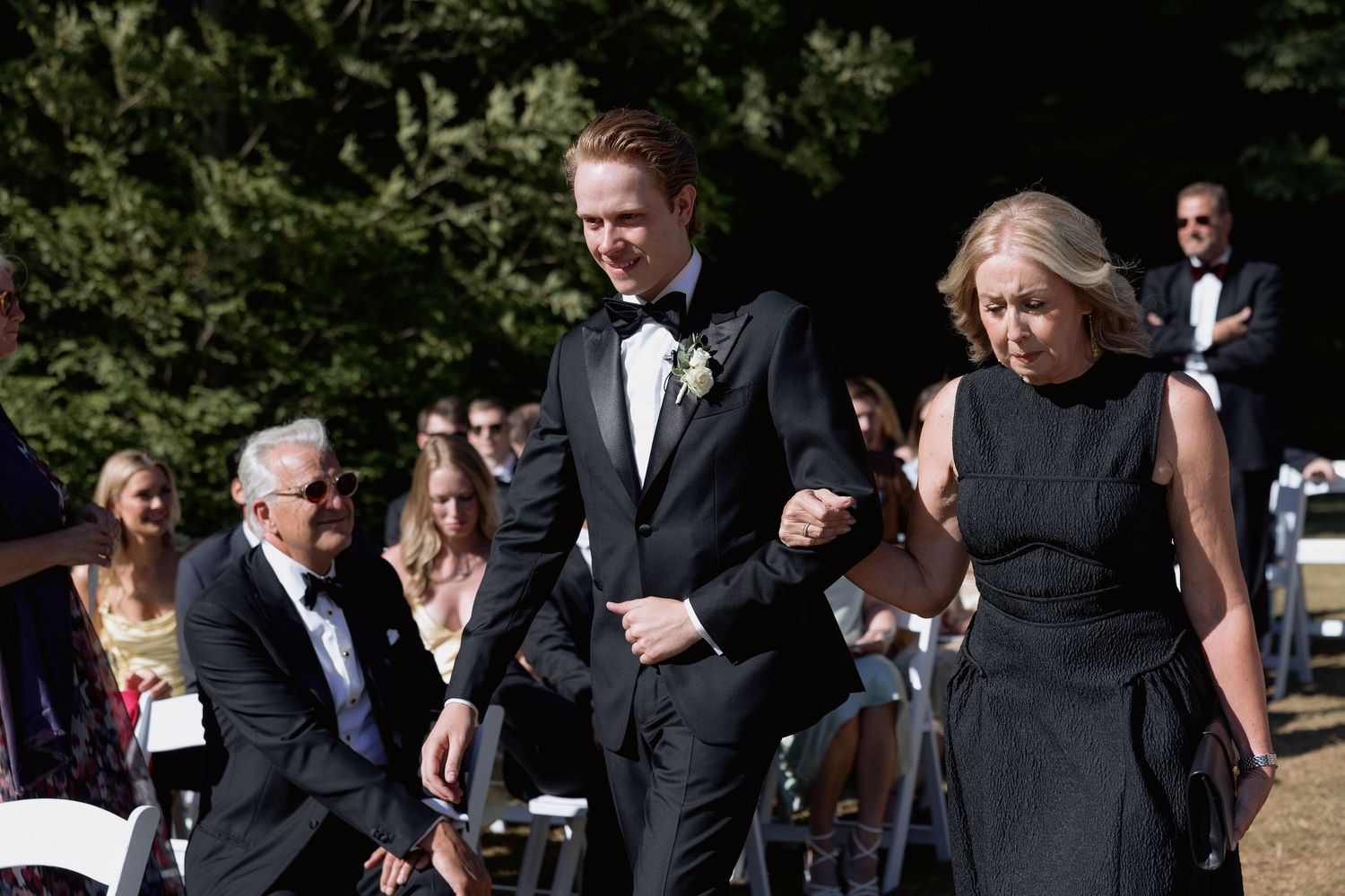 Guests mingle and socialize during an outdoor wedding reception on a sunny day.