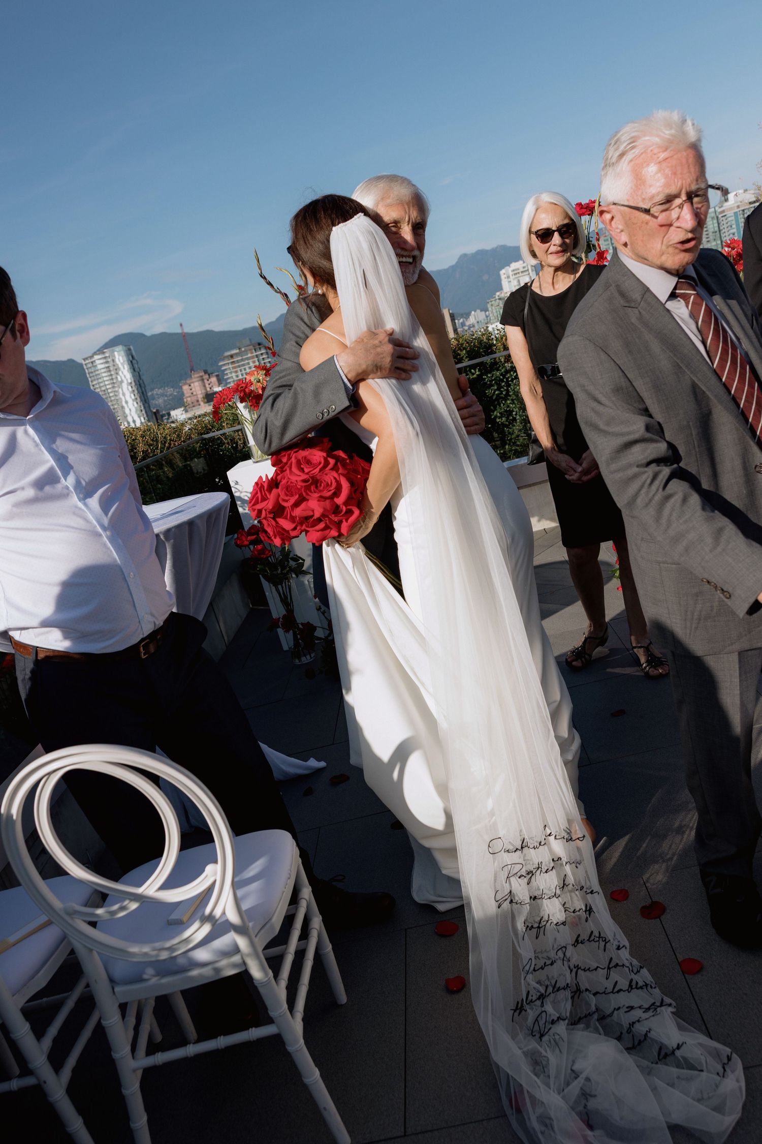 Elegant rooftop celebration with white chairs and red bouquets against an urban backdrop.