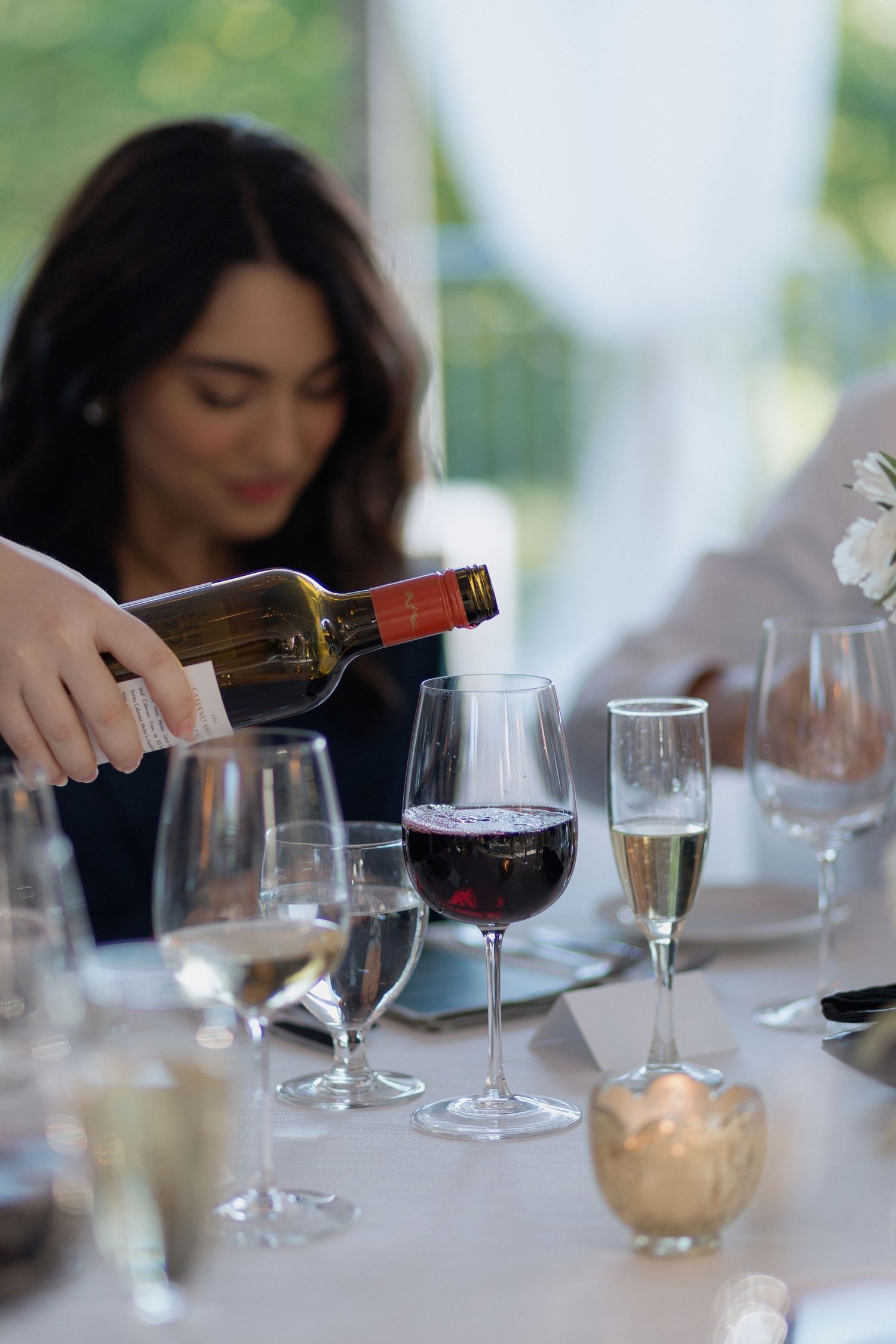 Wine glasses on a white tablecloth being filled during an elegant dinner service.