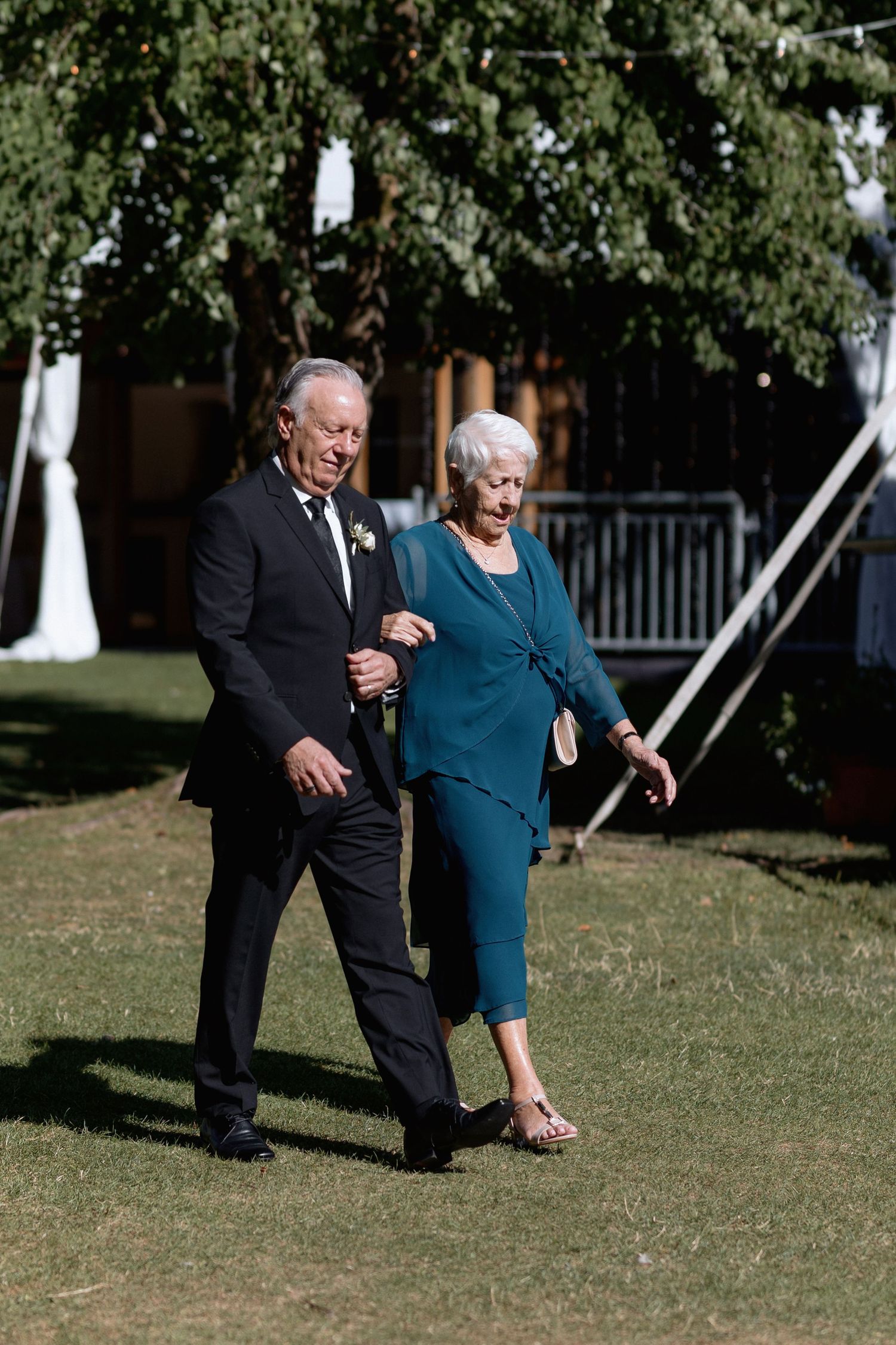 Wedding guests walking across sunny lawn in formal attire at outdoor venue.
