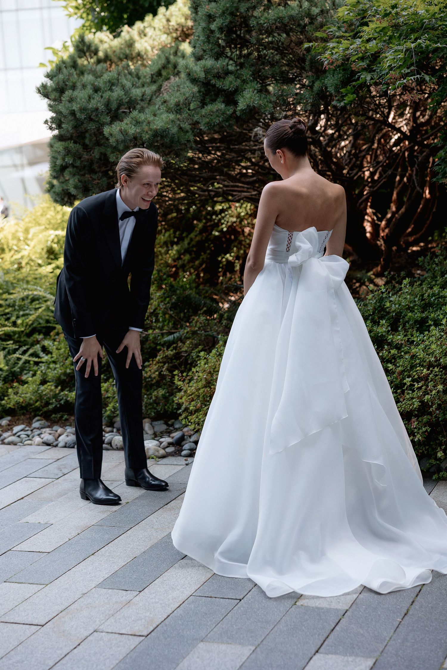 A wedding couple shares a candid moment on a stone pathway surrounded by evergreen bushes.