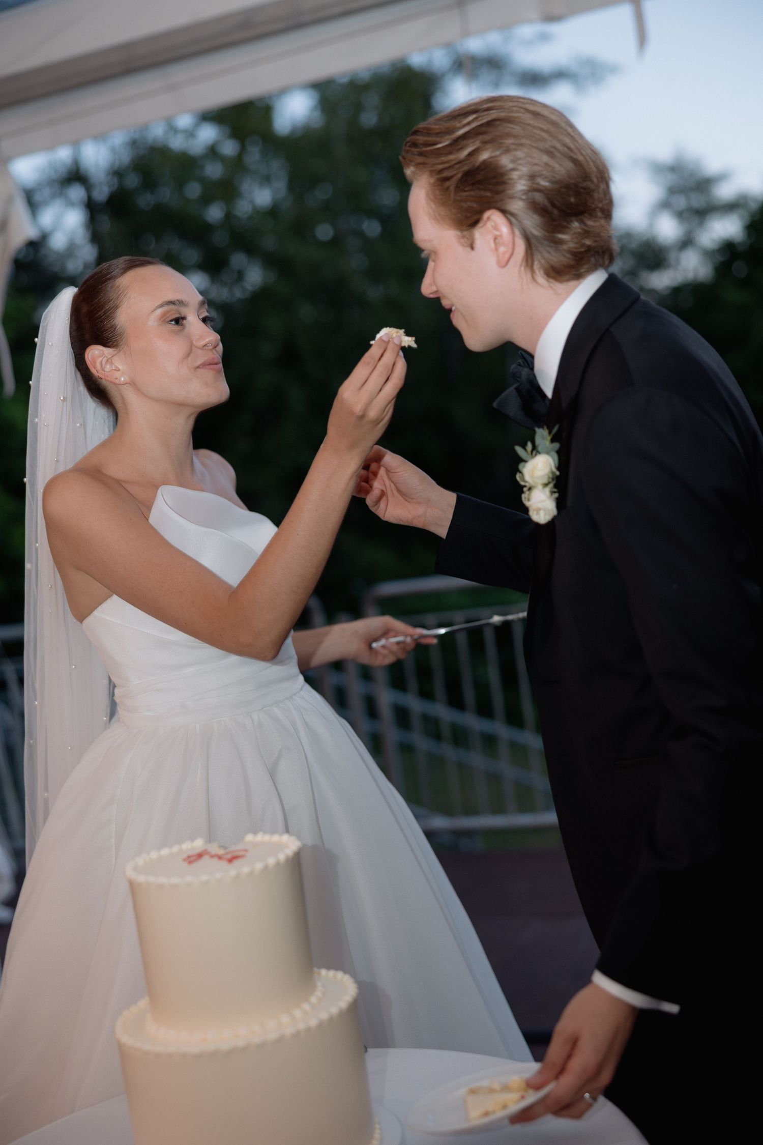 A playful cake-feeding moment between newlyweds at their outdoor reception.