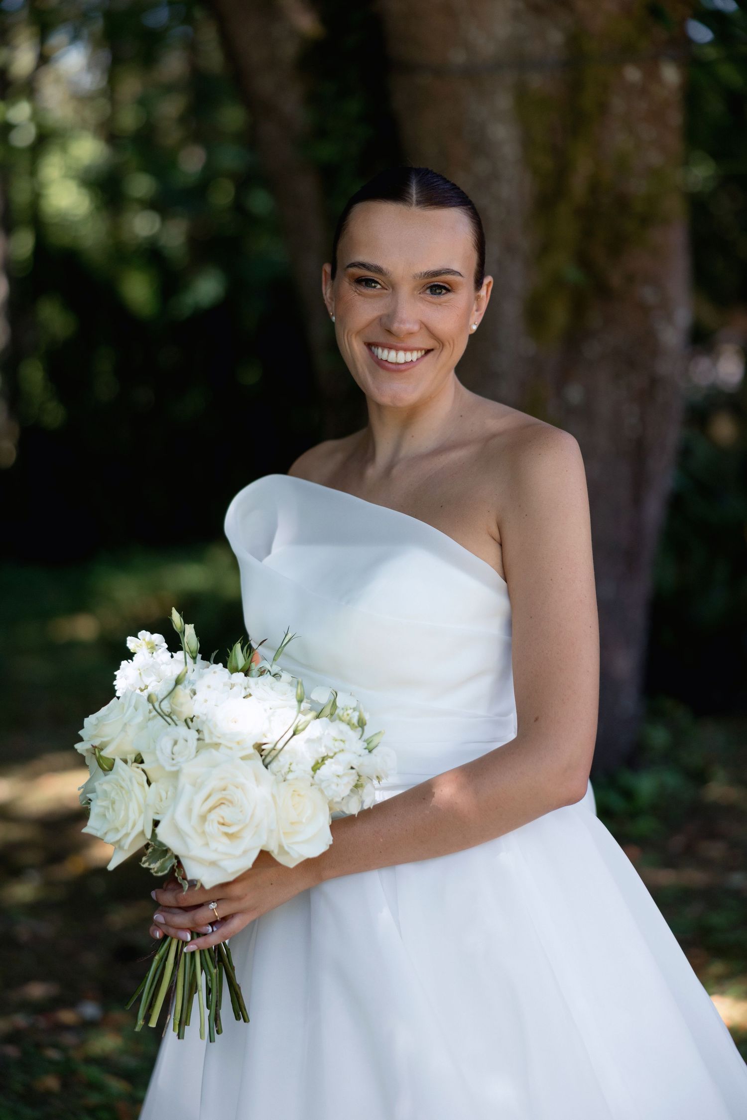 Person in strapless white wedding gown holding a classic white rose bouquet.