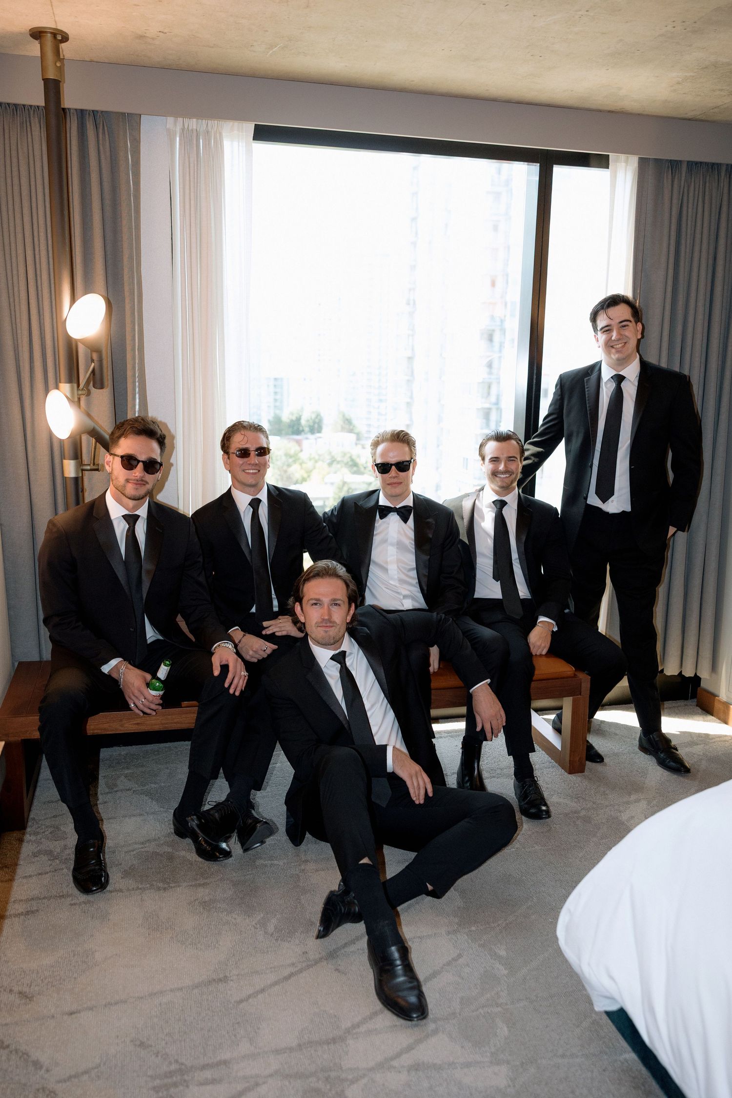Groomsmen in black suits posing casually in modern hotel room with large windows at Marriott Hotel in Vancouver