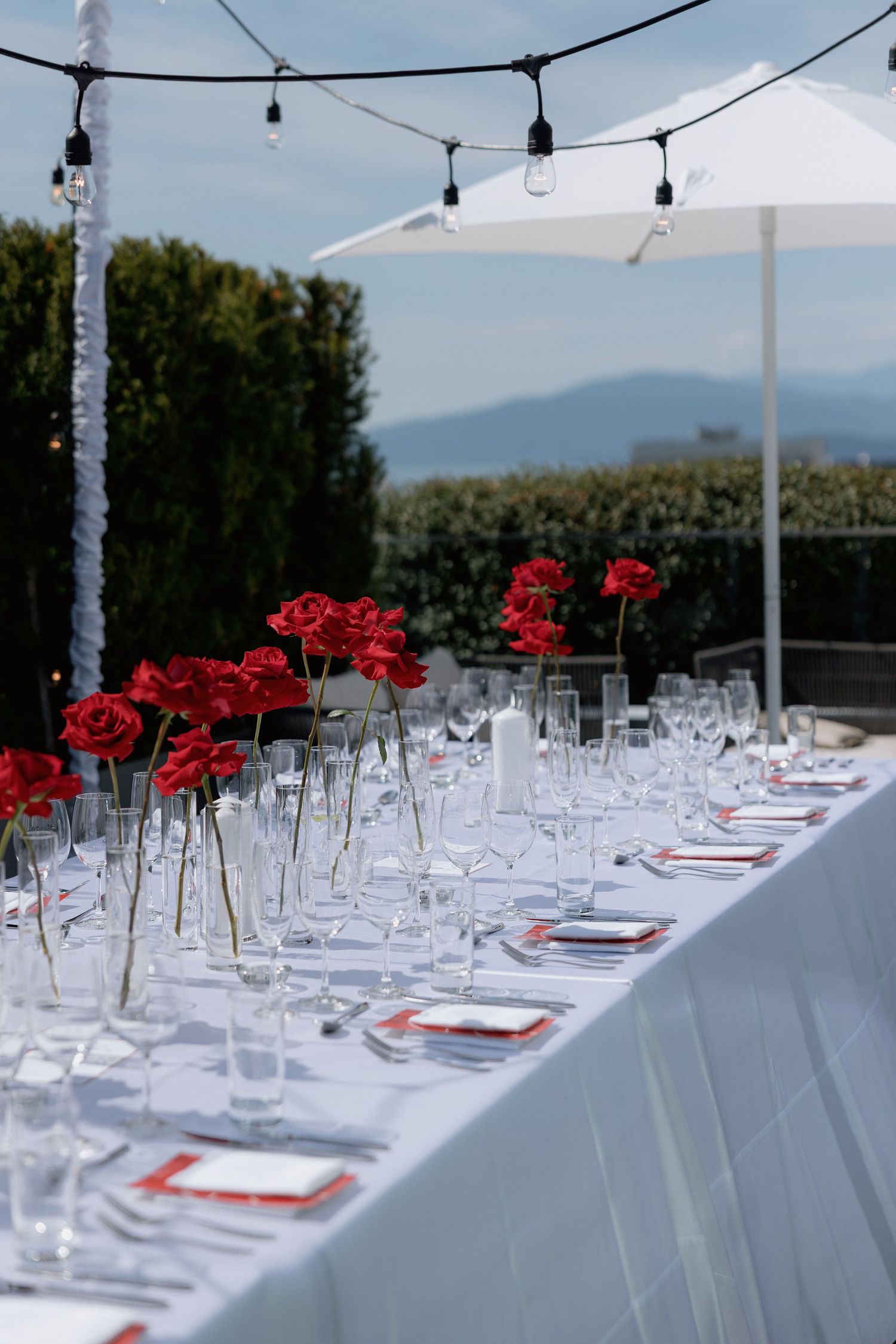 Outdoor wedding reception table setting with red roses and string lights under a white tent canopy.
