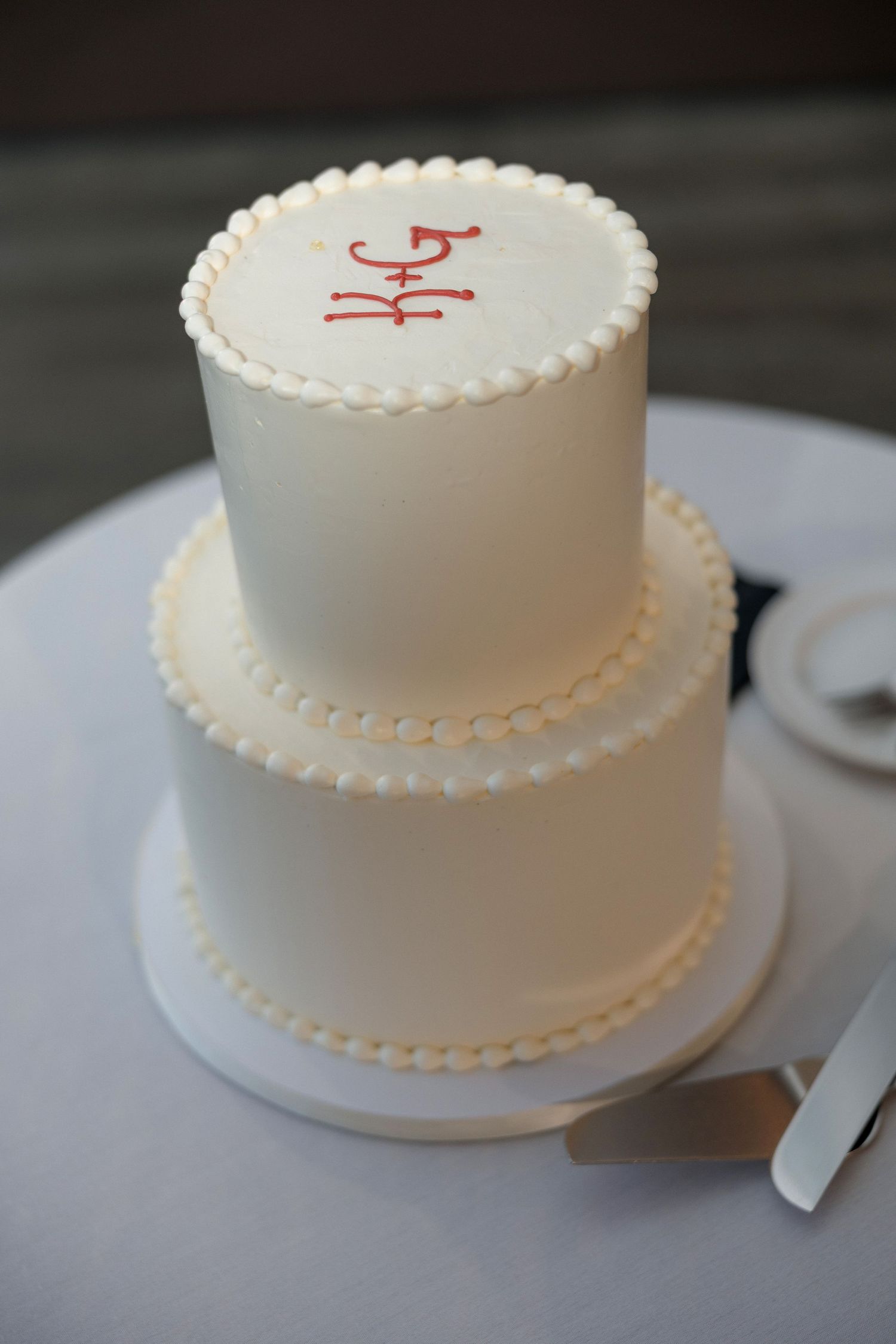 A simple two-tier white wedding cake with delicate pearl piping decoration.