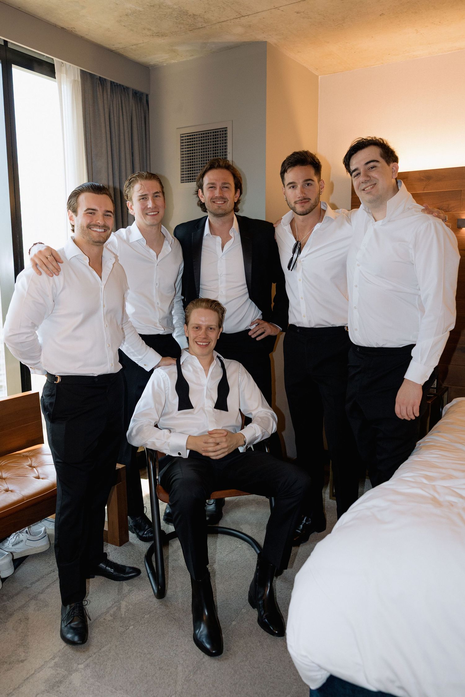 Wedding party members in formal attire gathered on a hotel room bed.