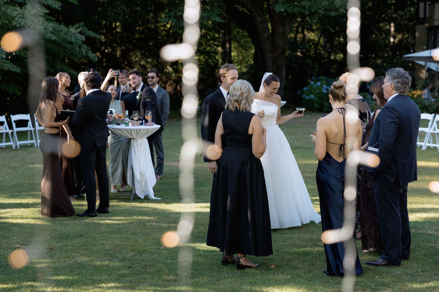 Wedding guests enjoying cocktail hour on a lawn with string lights overhead.