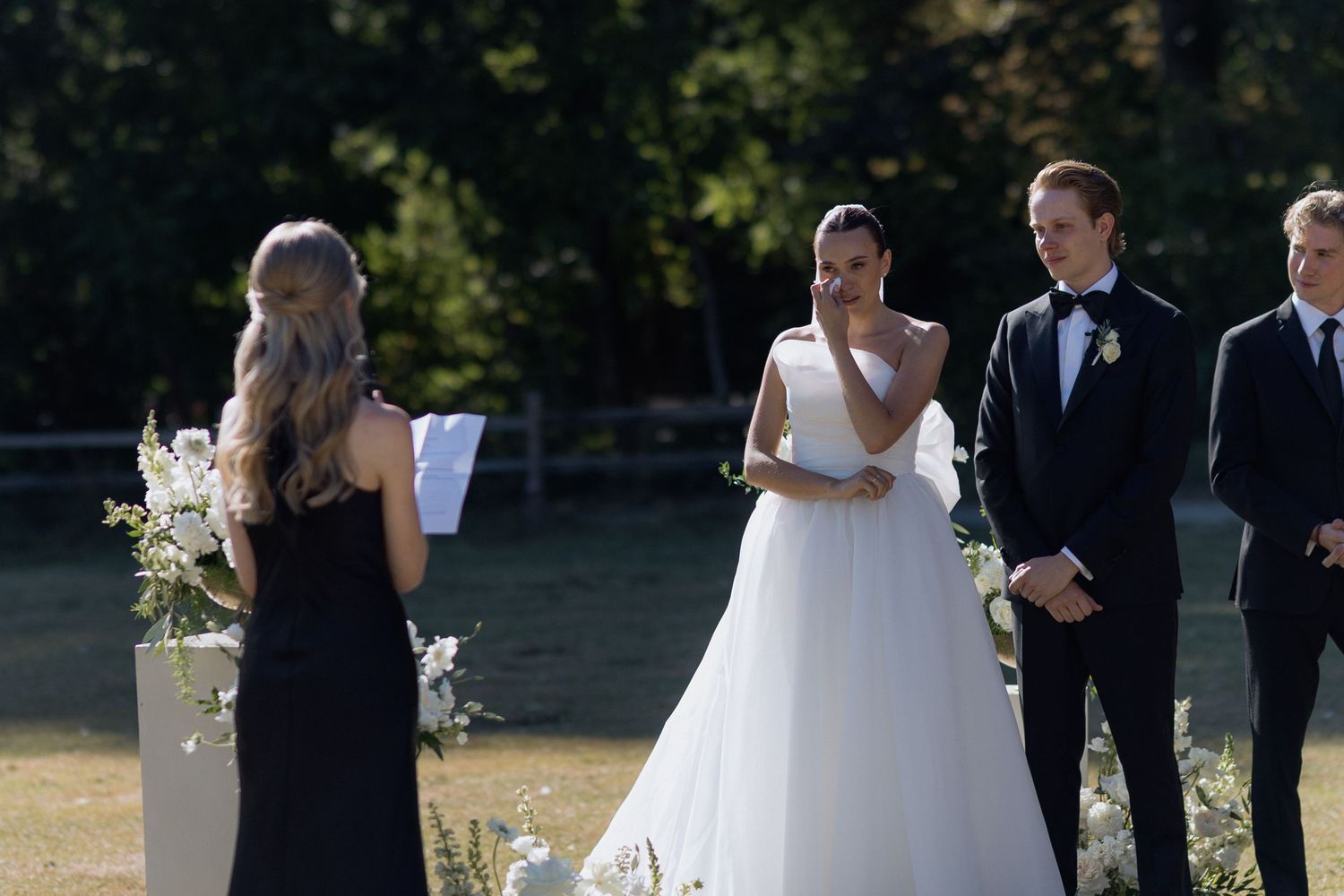 Wedding ceremony in progress with white floral arrangements and guests in formal attire.
