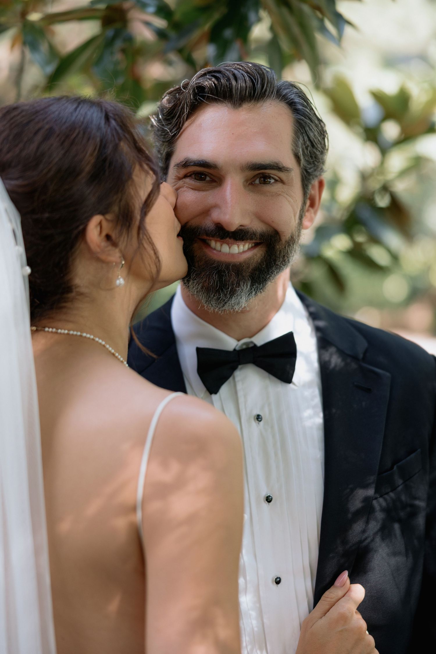 Intimate wedding portrait showing tender moment between newlyweds against natural foliage background.