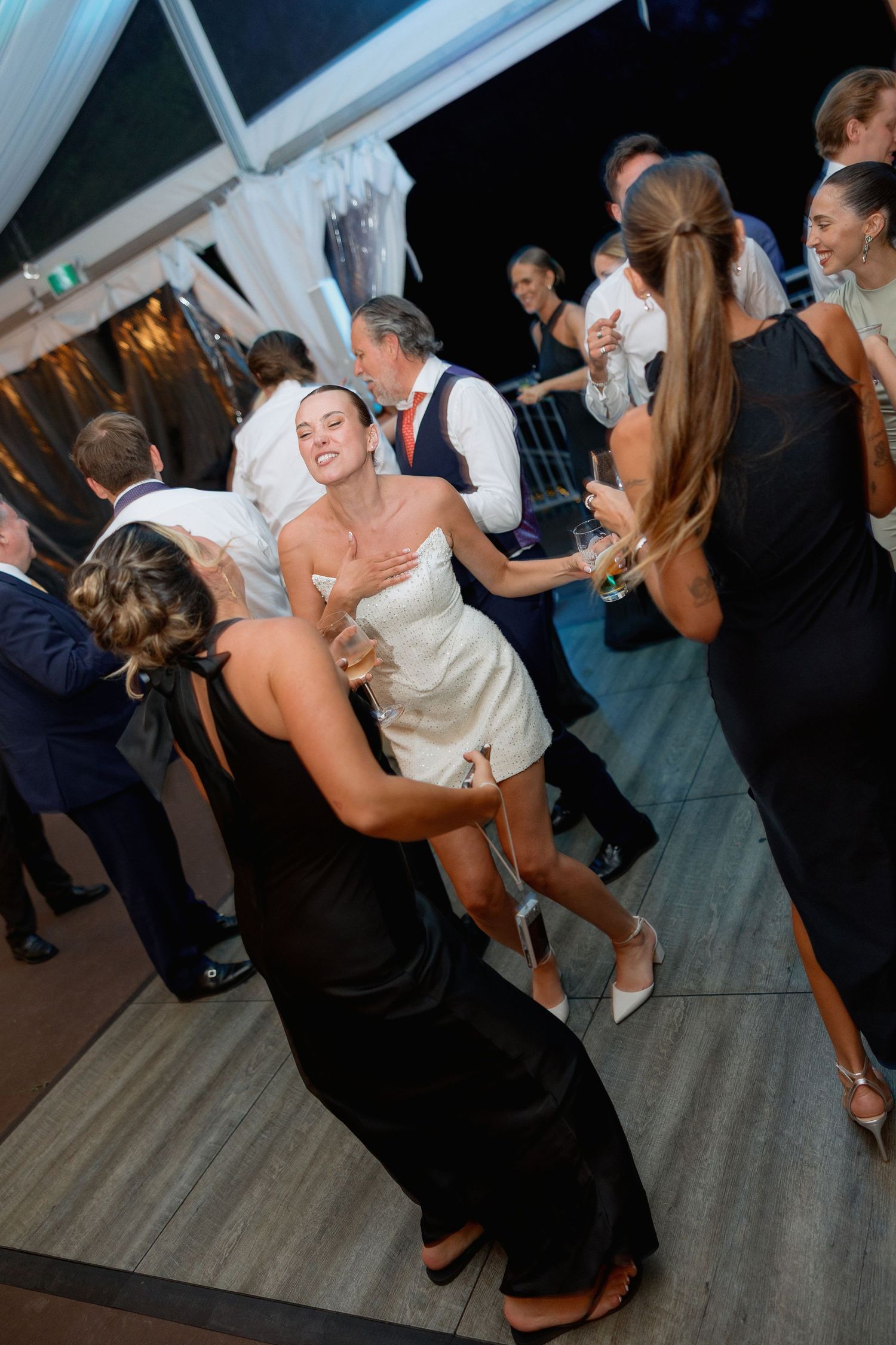 Wedding guests dancing and celebrating on a dark wooden dance floor at night.