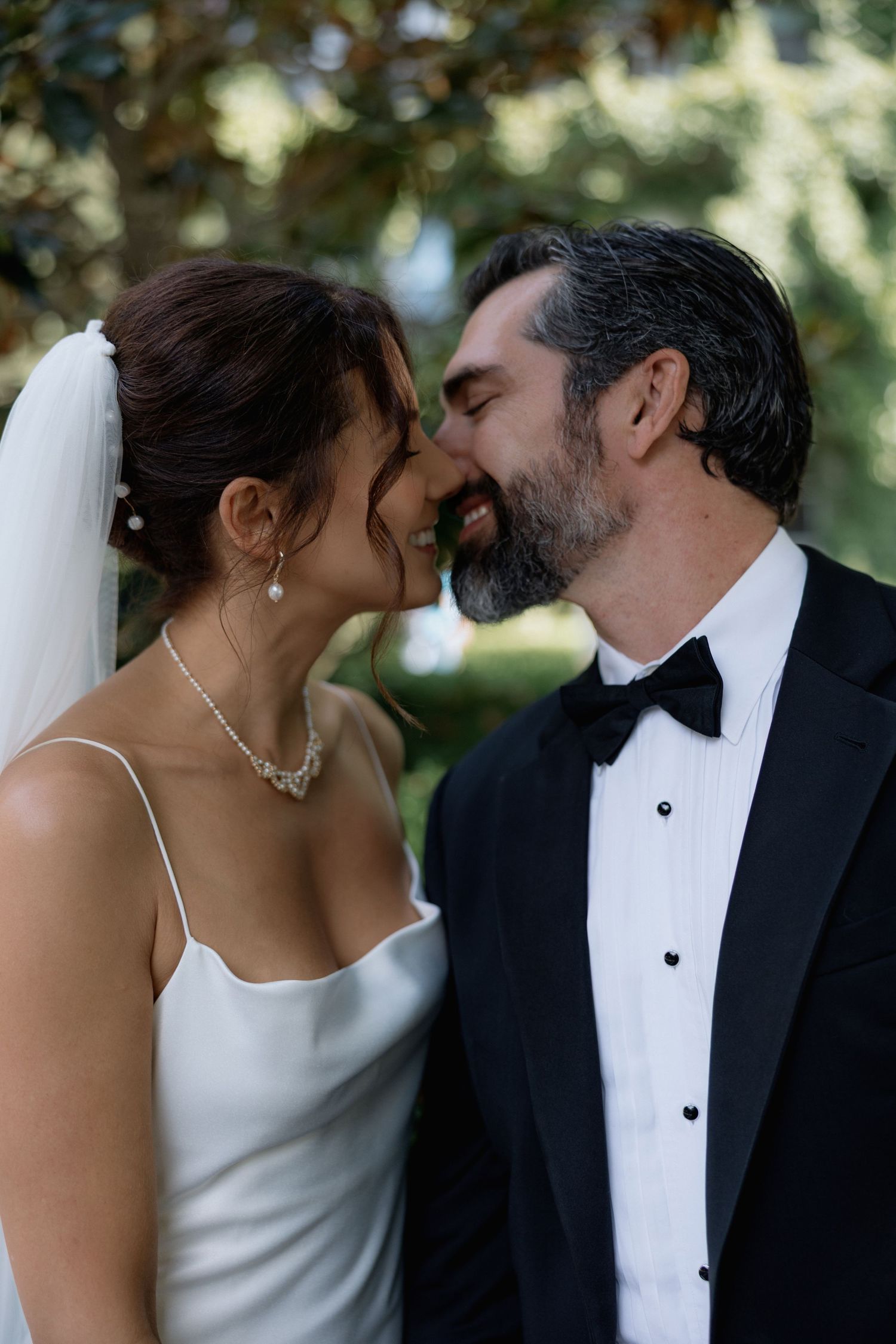 A romantic wedding moment captured outdoors with a bride in white and groom in tuxedo sharing an intimate moment.