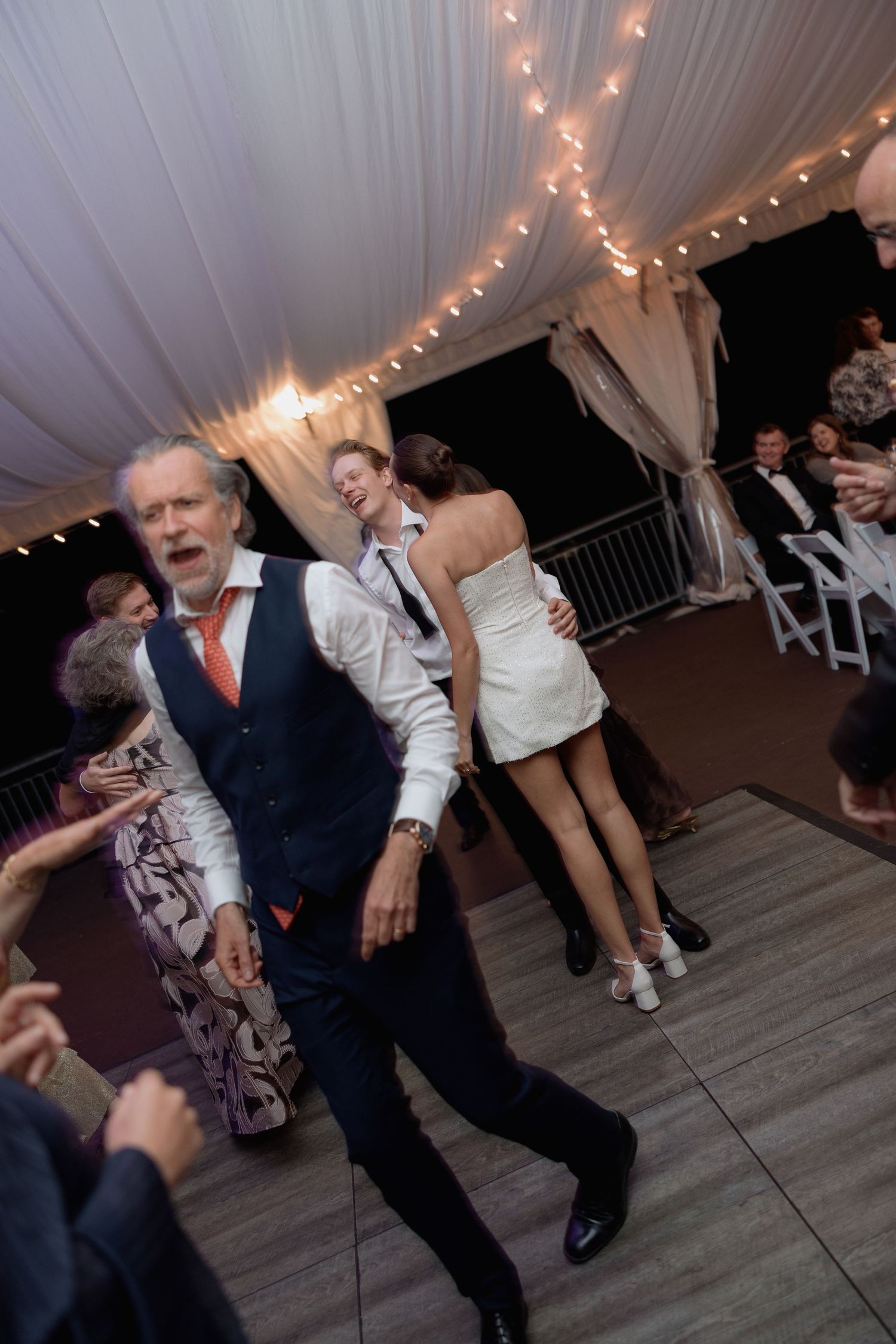 Guests showing off dance moves at a lively wedding reception under string lights.