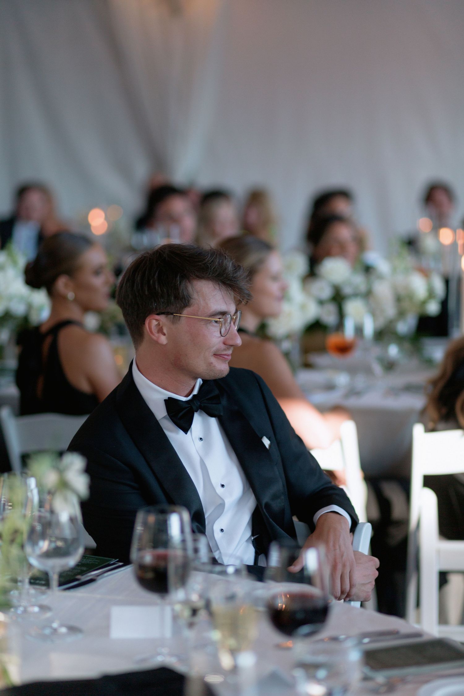 Formal dinner guests in black tie attire seated at decorated reception tables.