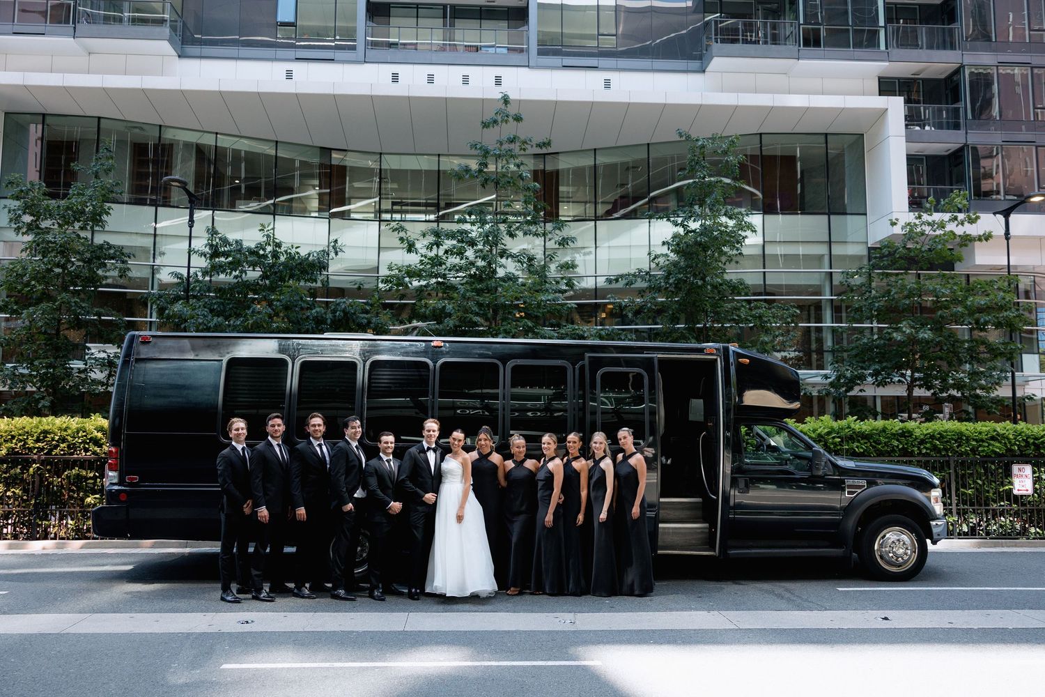 Wedding party poses near luxury limousine outside modern glass building complexat Marriott Hotel in Vancouver