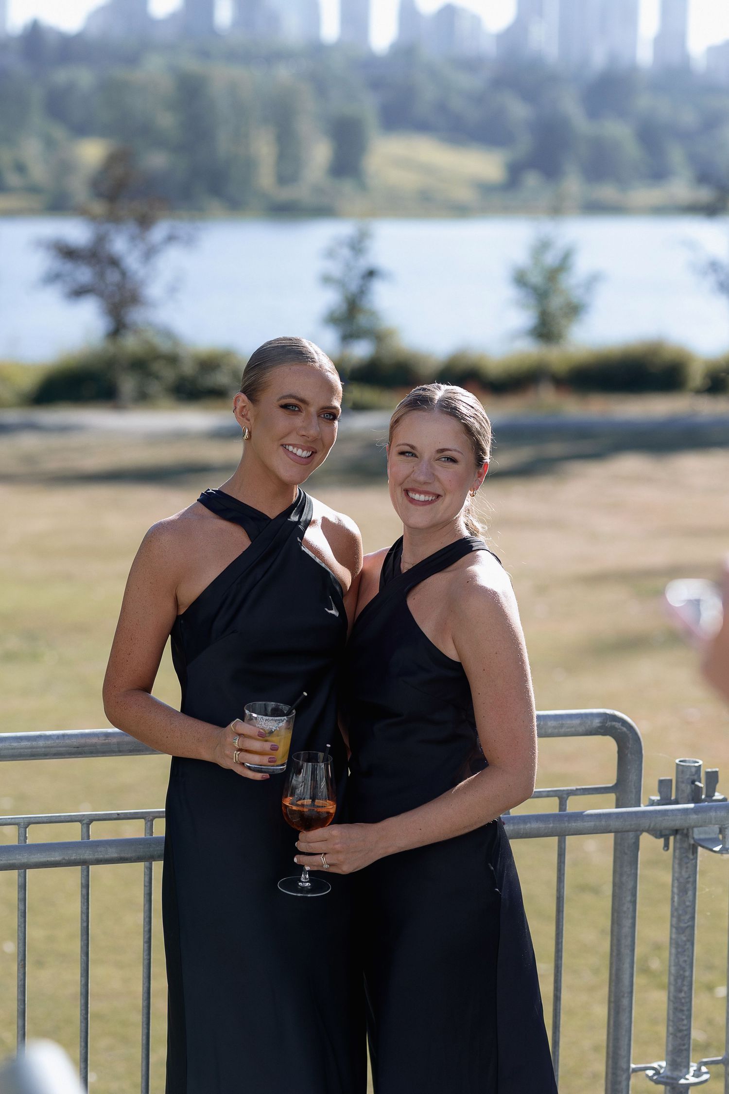 Two people in black dresses share a moment on a deck overlooking water Deer Lake
