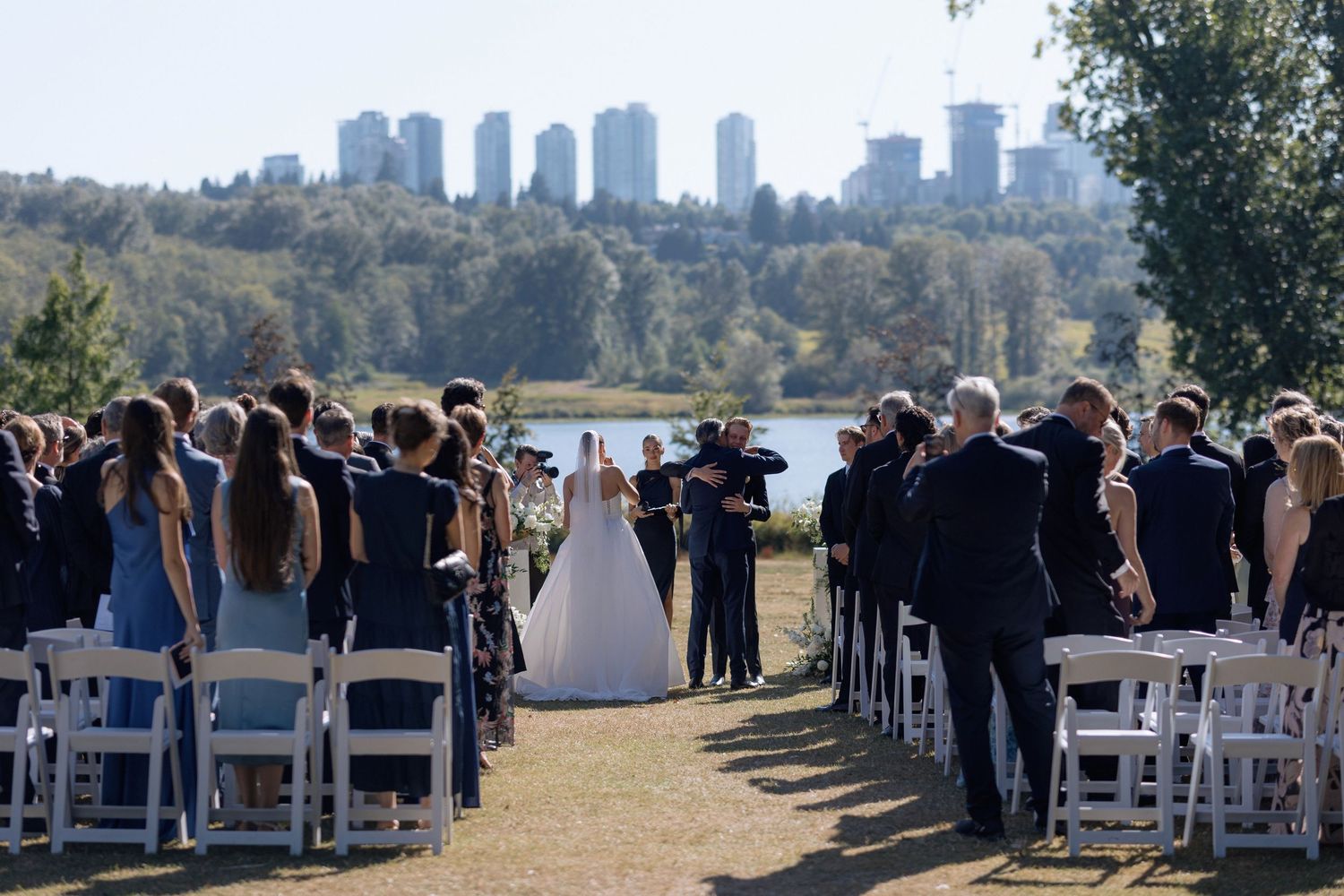 Outdoor wedding ceremony setup with white chairs and city skyline backdrop on a sunny day at Hurt House in Burnaby