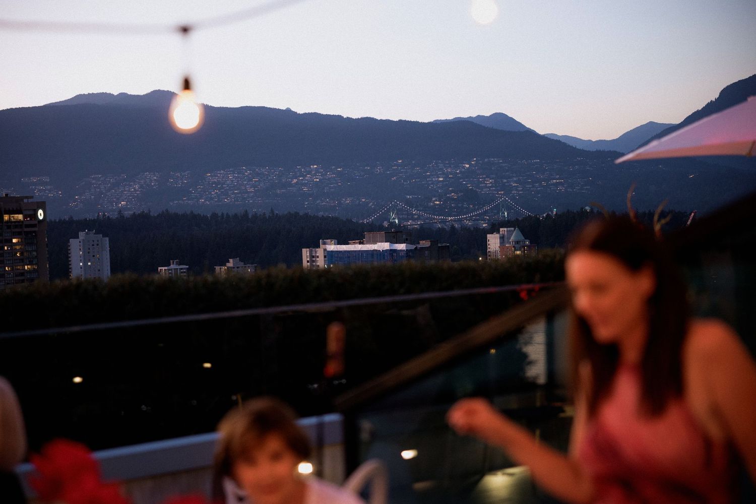 Mountain silhouettes at dusk during outdoor rooftop celebration with string lights with mountain backdrop in Vancouver