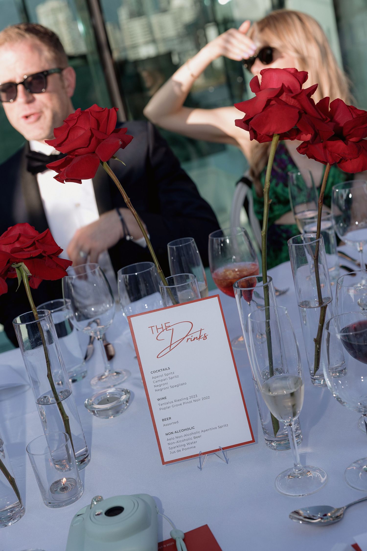 Table setting with red roses, wine glasses and menu cards for an outdoor celebration.