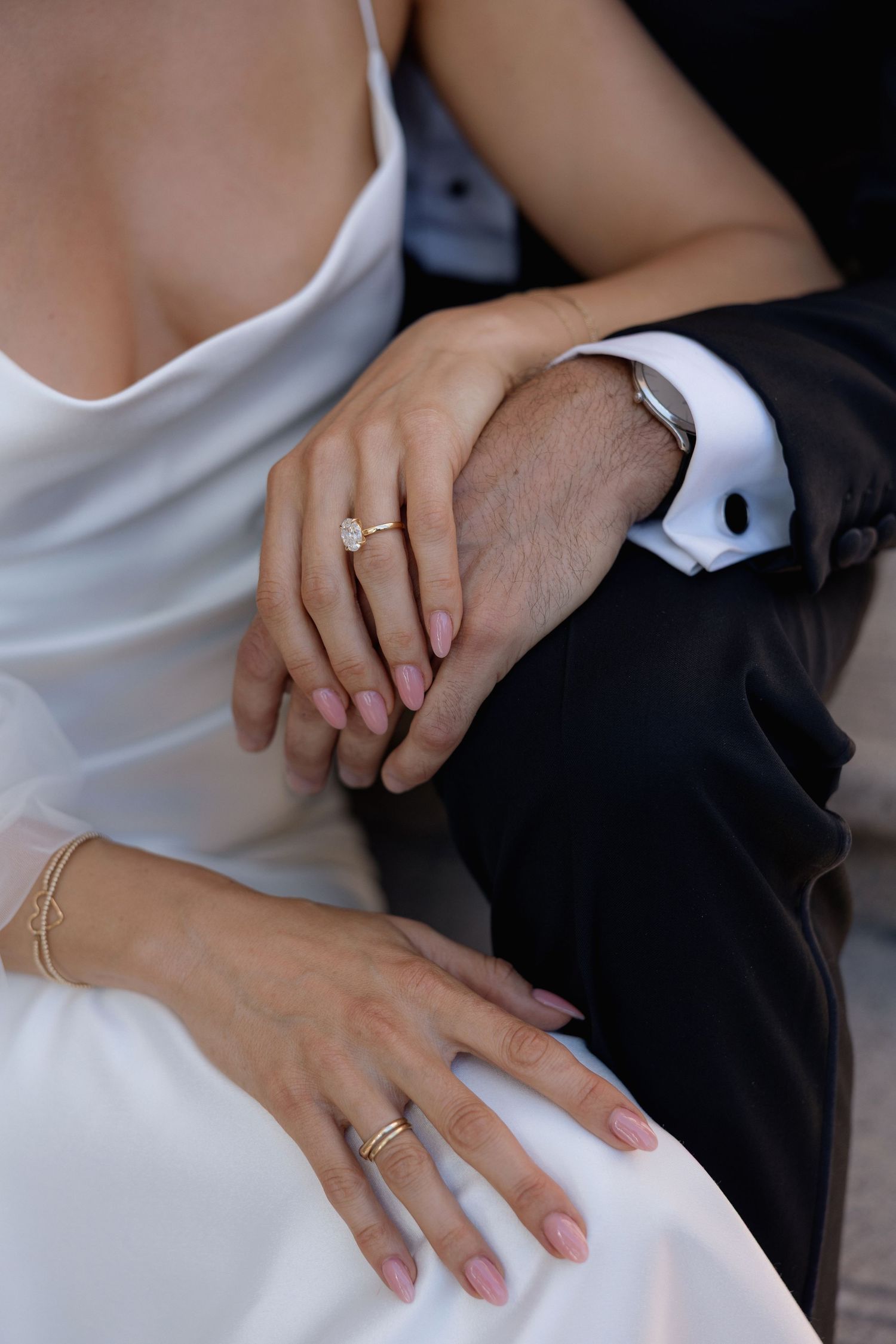 Close-up of wedding rings and clasped hands showing elegant bridal manicure.