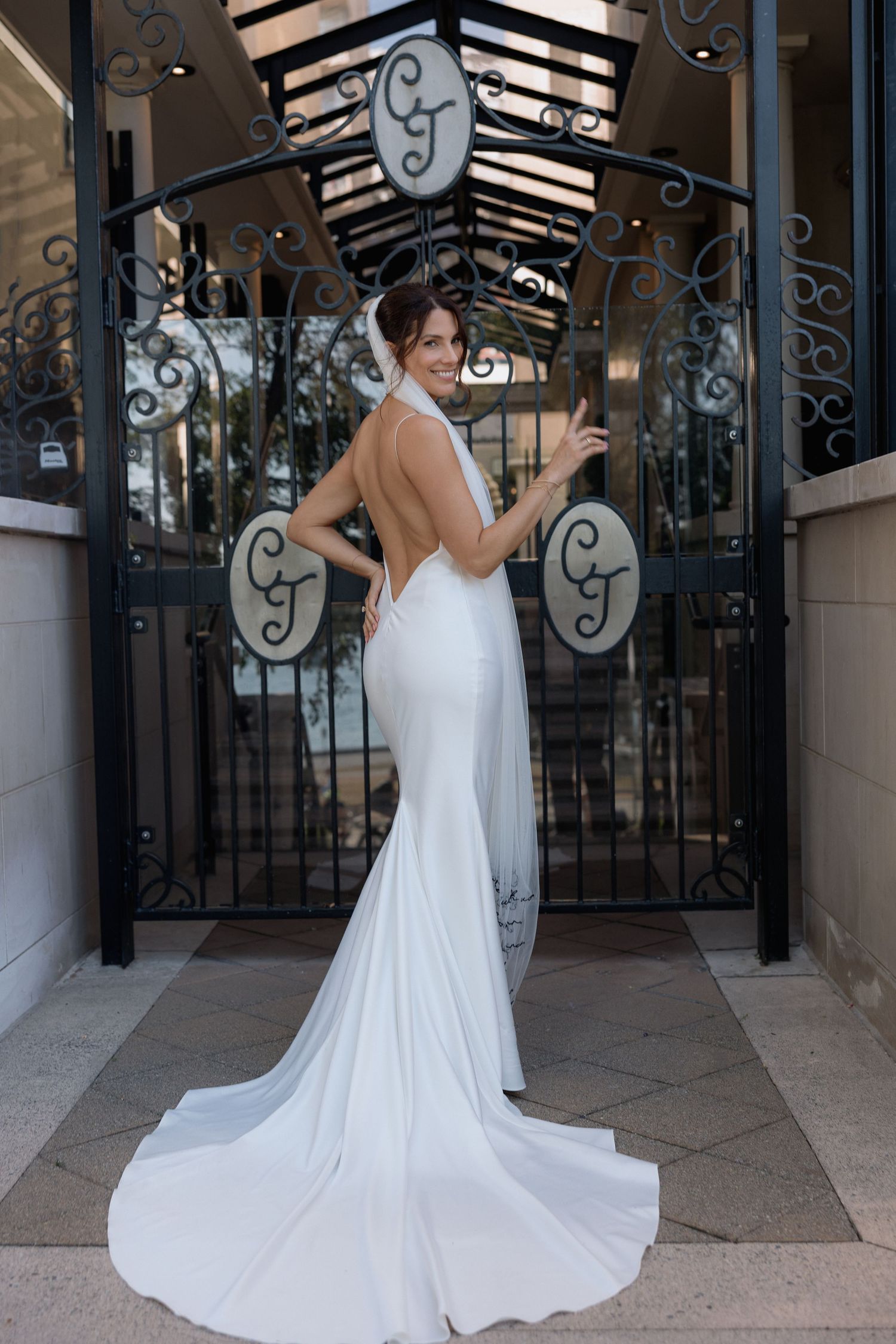 Elegant backless white wedding gown with flowing train photographed at ornate iron gateway entrance.