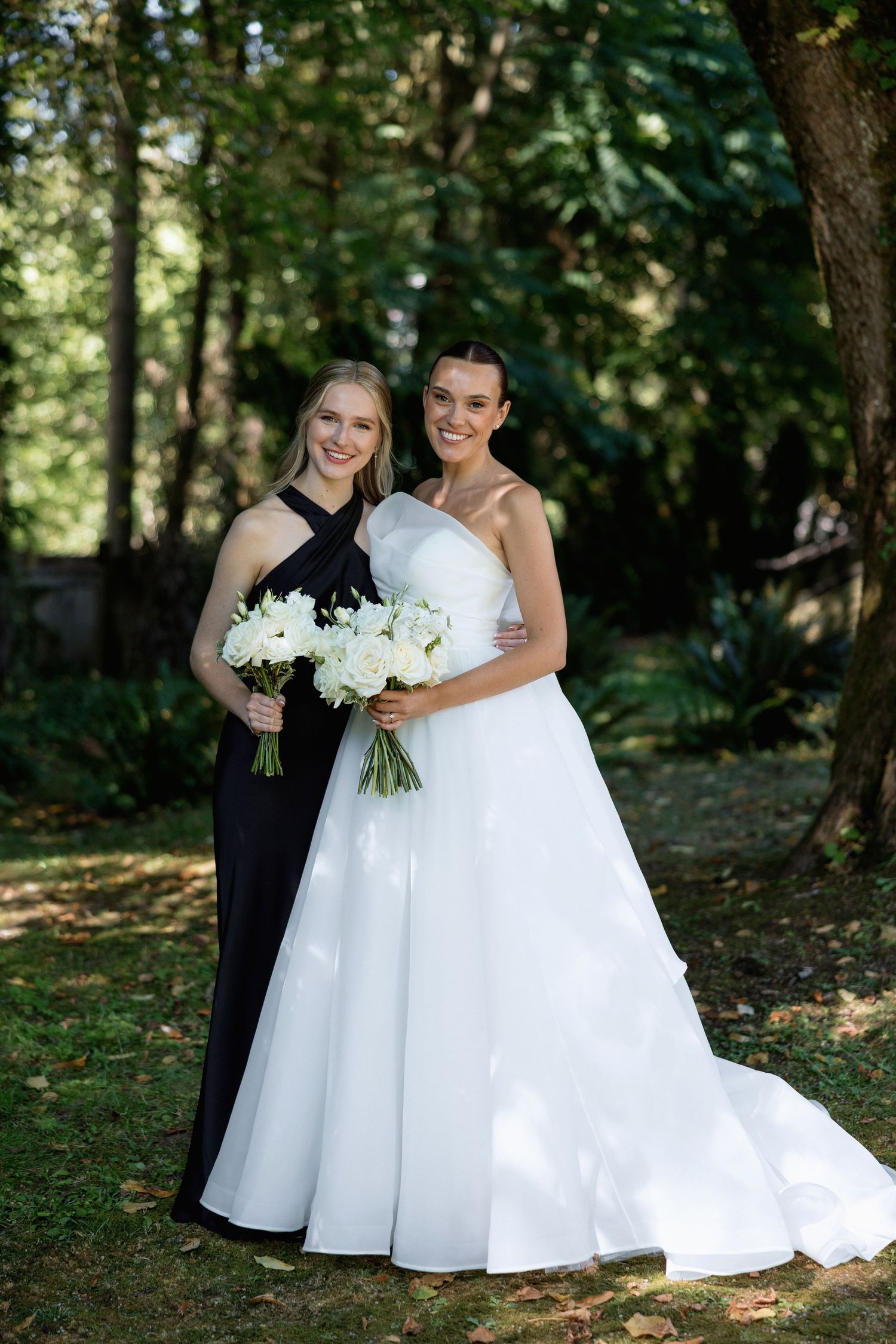 Outdoor wedding photo with two people posing together holding white floral bouquets.