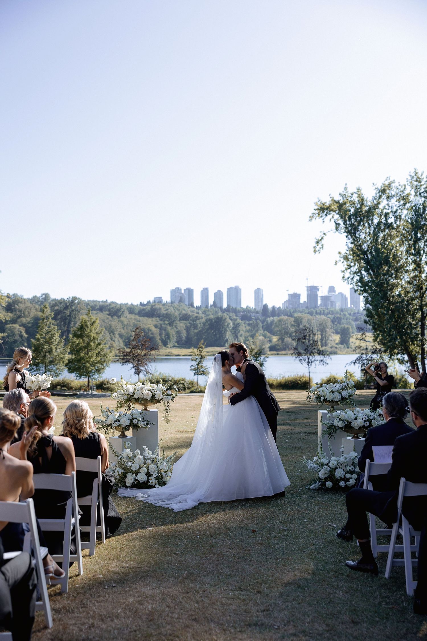 Outdoor wedding ceremony setup with white chairs and floral arrangements overlooking a scenic waterfront Deer Lake