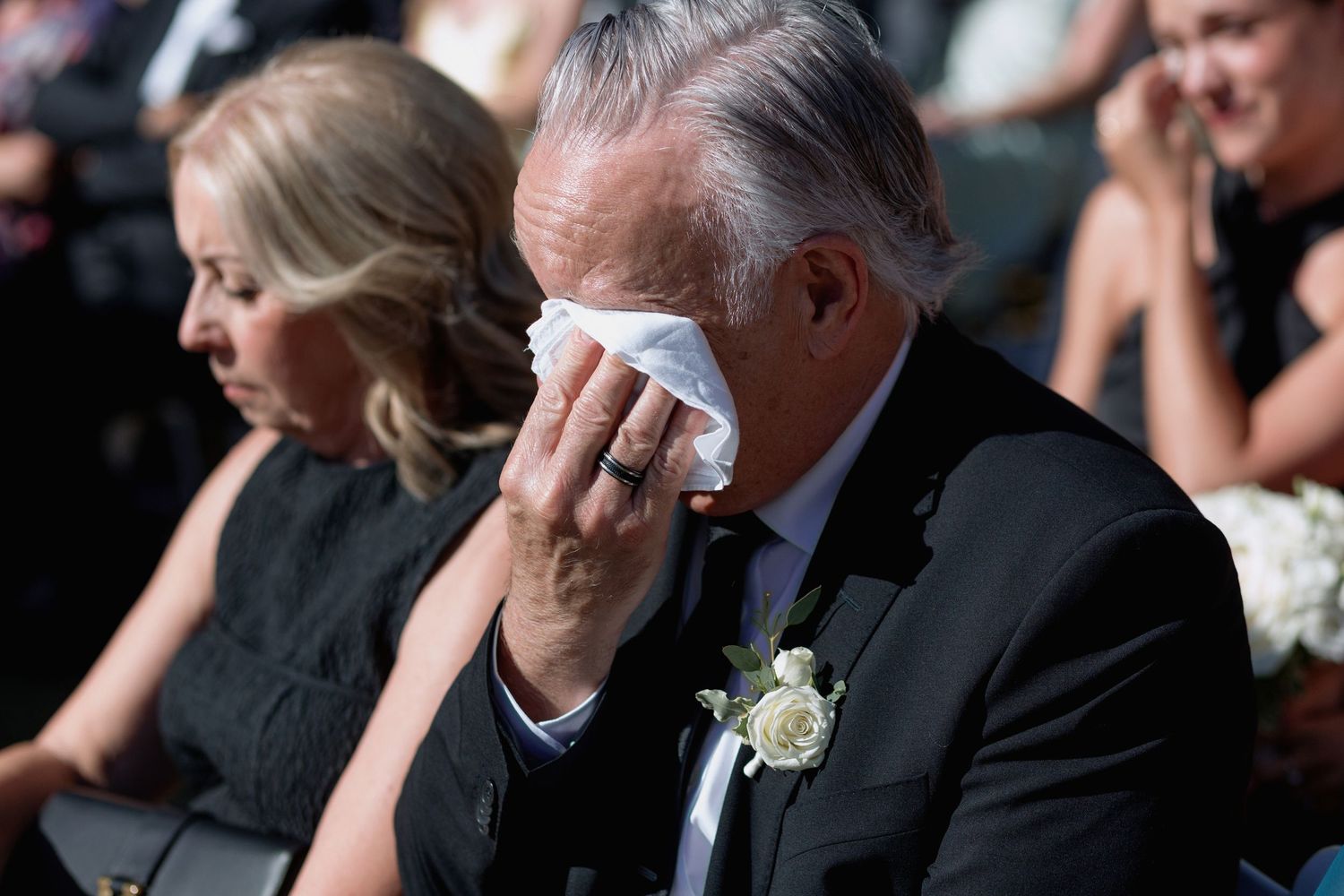 Wedding guests react emotionally during a ceremony, wiping away tears while seated in formal attire.