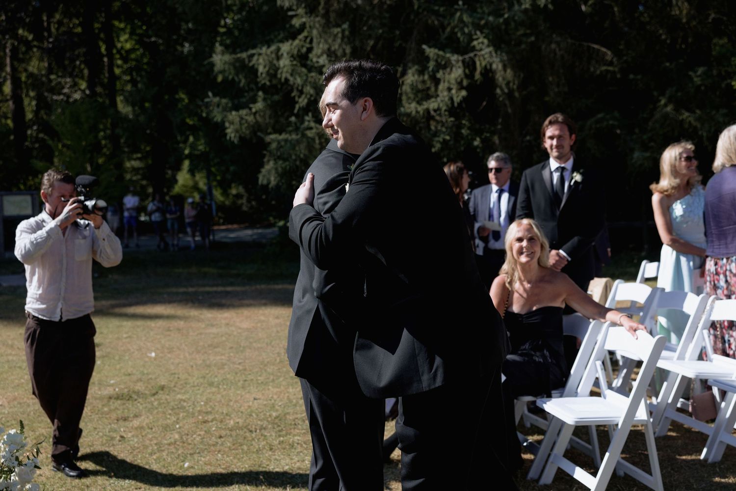 Wedding ceremony setup in a park with white chairs and guests gathering.