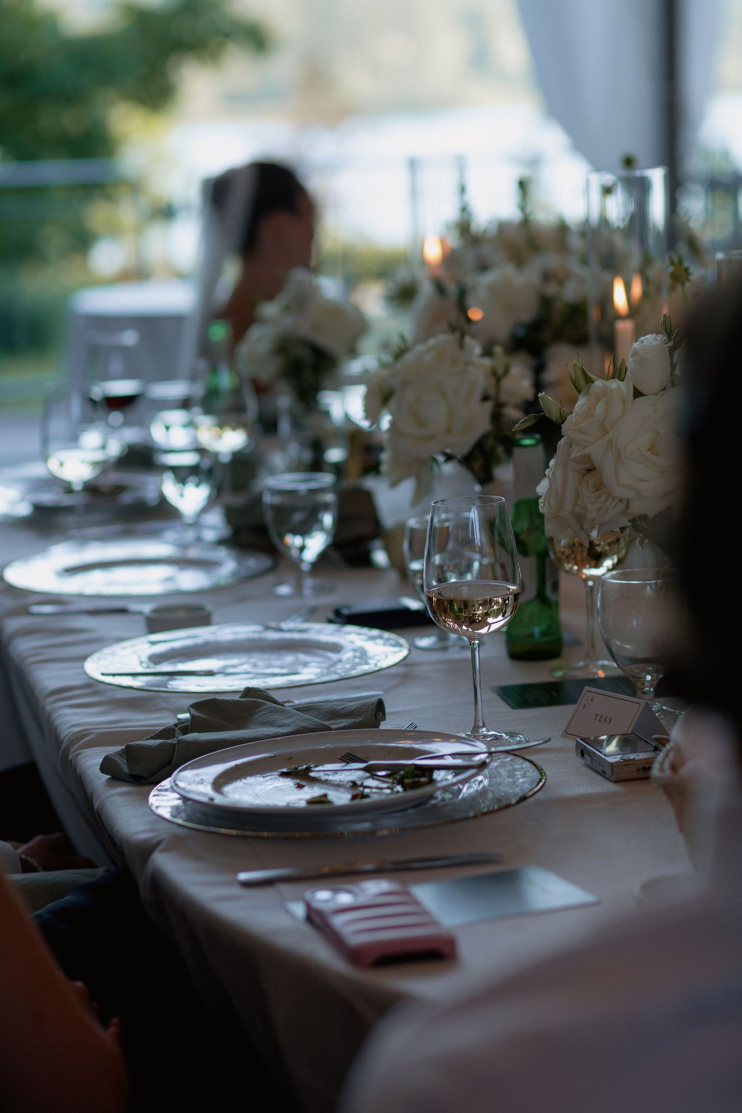 Elegant table settings with white plates, wine glasses and floral centerpieces at wedding reception.