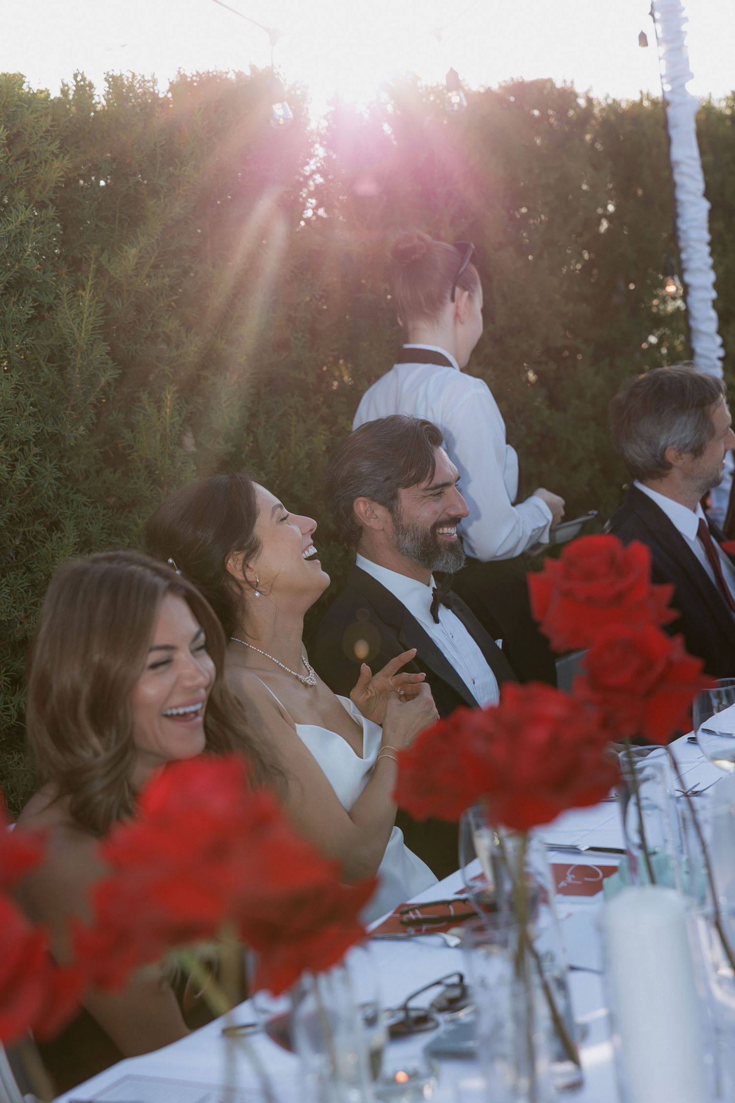 Wedding reception table with red floral centerpieces during golden hour sunset.