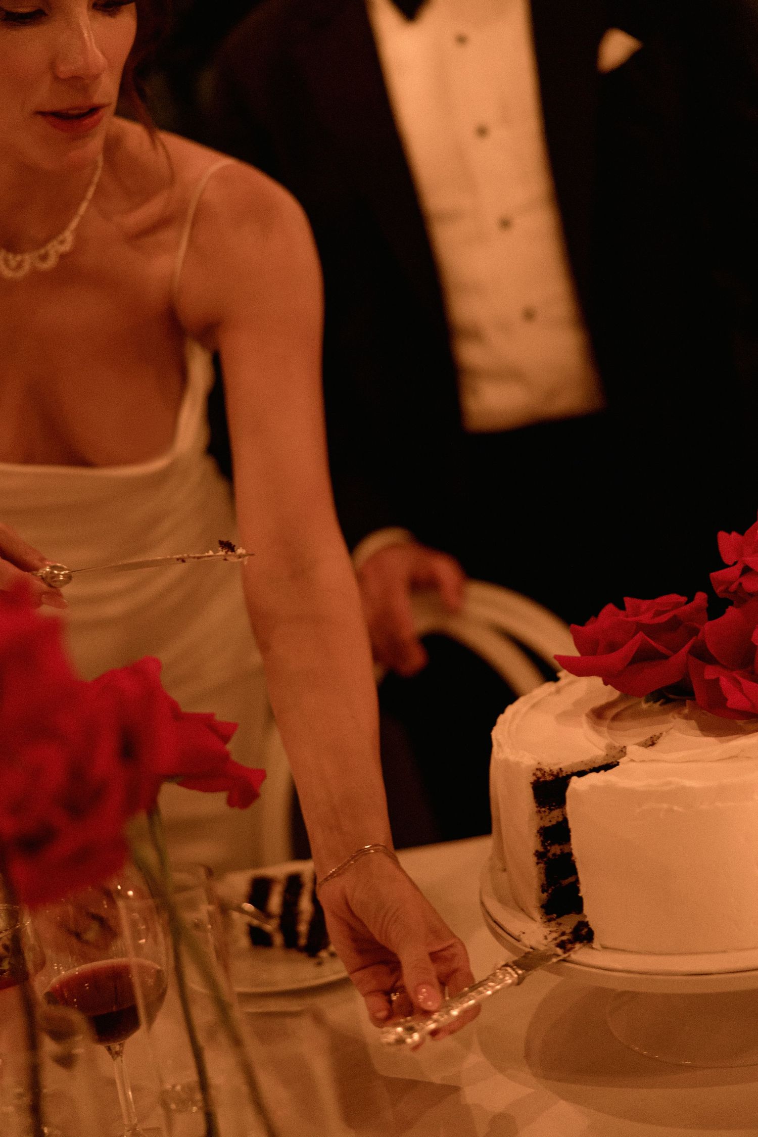 Wedding cake decorated with red roses captured in warm candlelight in Vancouver