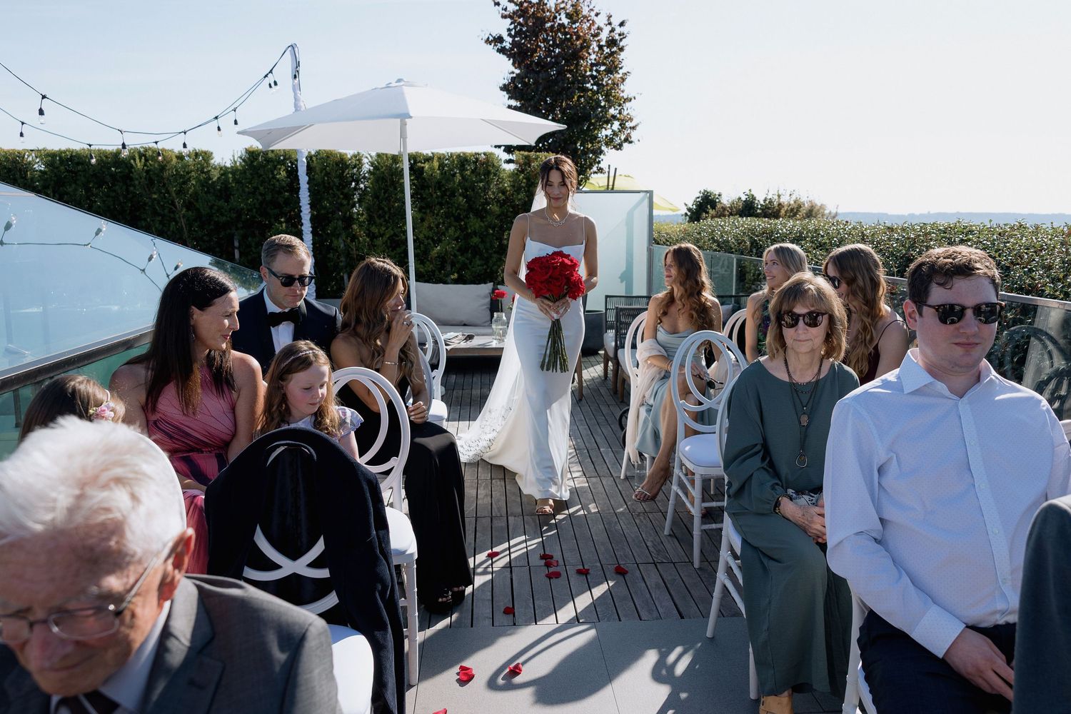 Wedding guests mingling at an outdoor rooftop reception with white umbrellas.