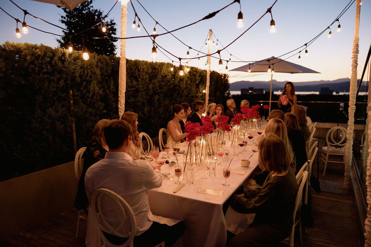 String lights illuminate an outdoor wedding reception dinner setup at dusk in Vancouver