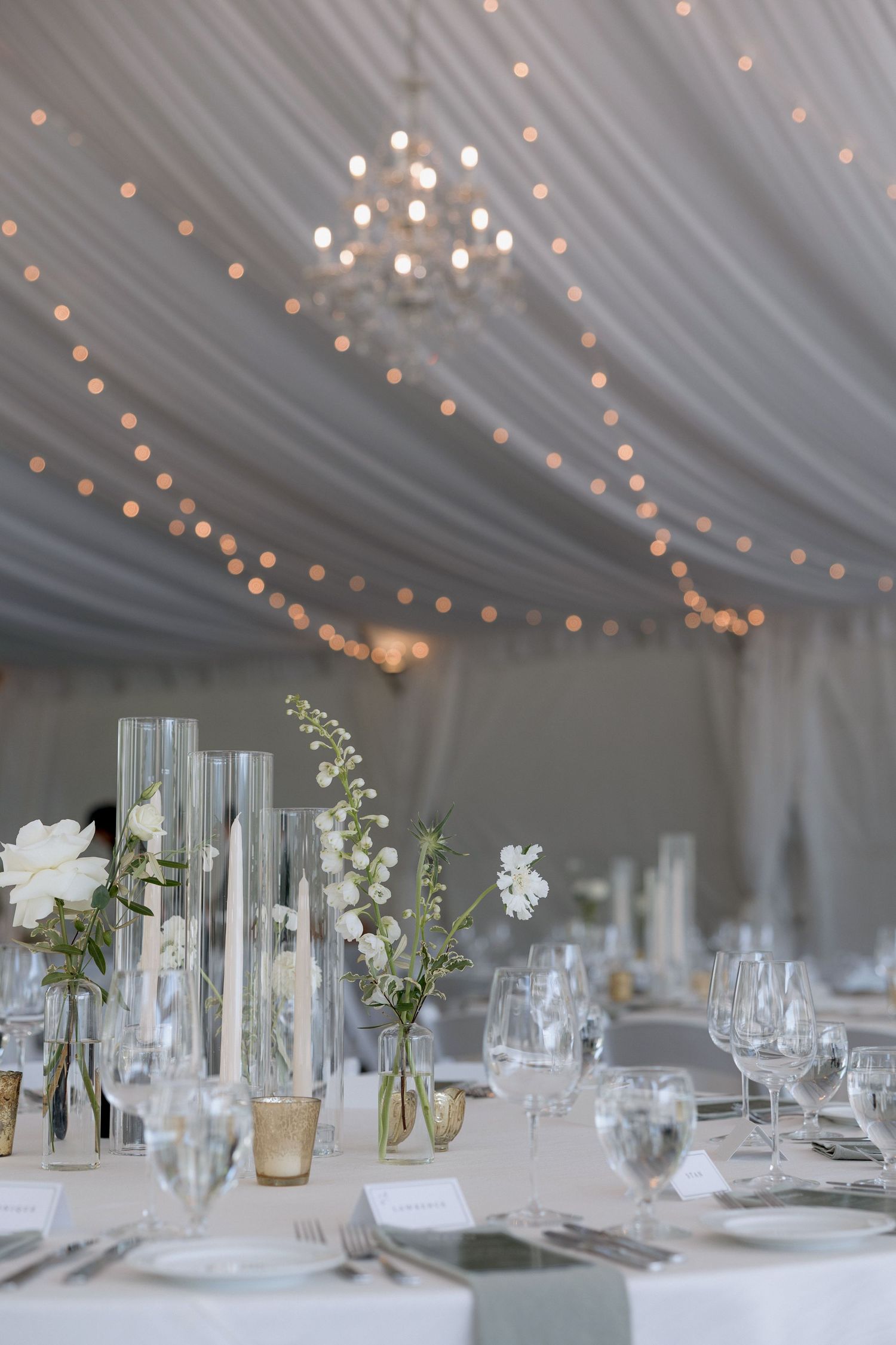 White fabric draped ceiling with twinkling string lights and elegant table settings below.