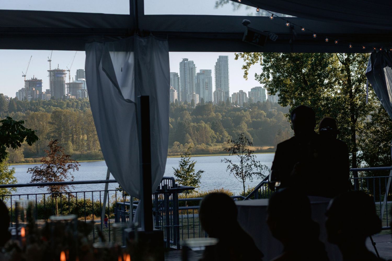 Elegant outdoor wedding venue with city skyline view through draped tent and trees at sunset.