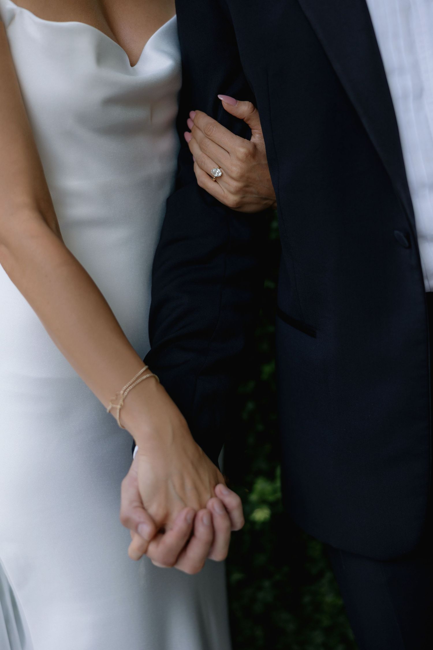 Close-up of couple's hands during wedding ceremony showing elegant white dress, dark suit, and sparkling engagement ring.