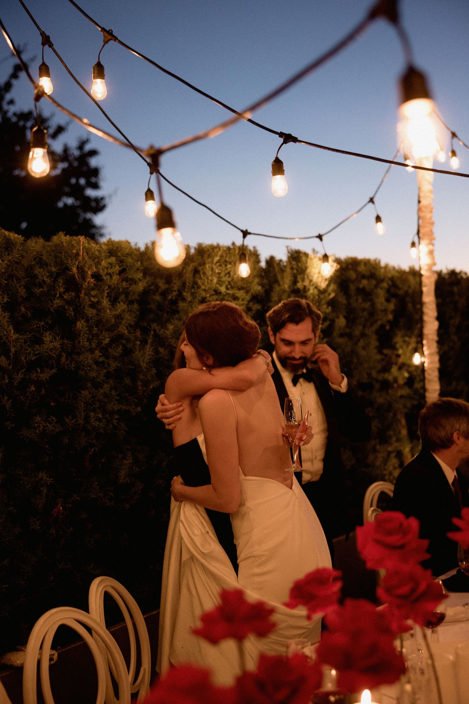 Wedding couple dancing under romantic string lights at an outdoor evening reception.