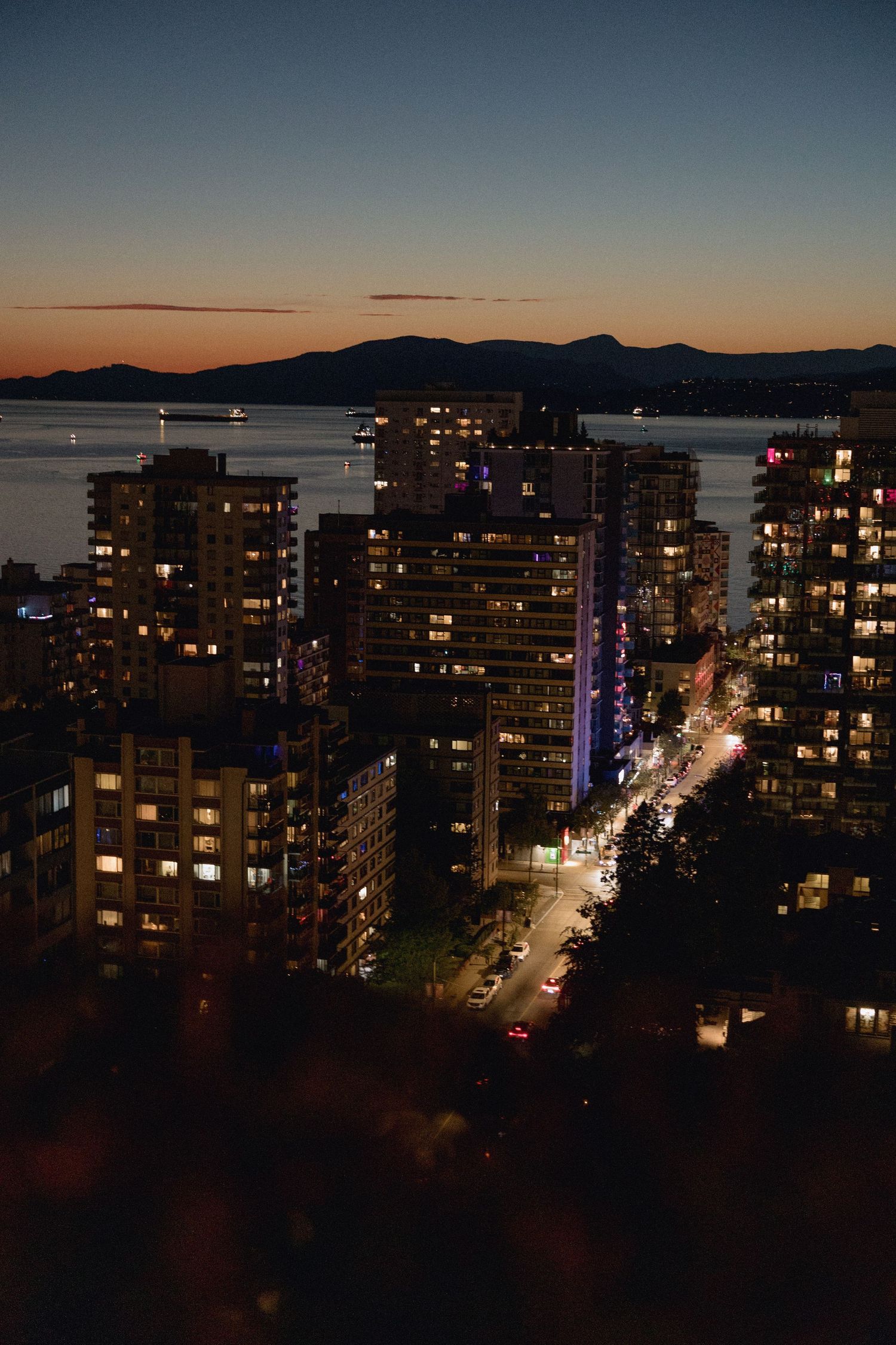 Night view of city streets of Vancouver and high-rise buildings with mountains visible in the distance.