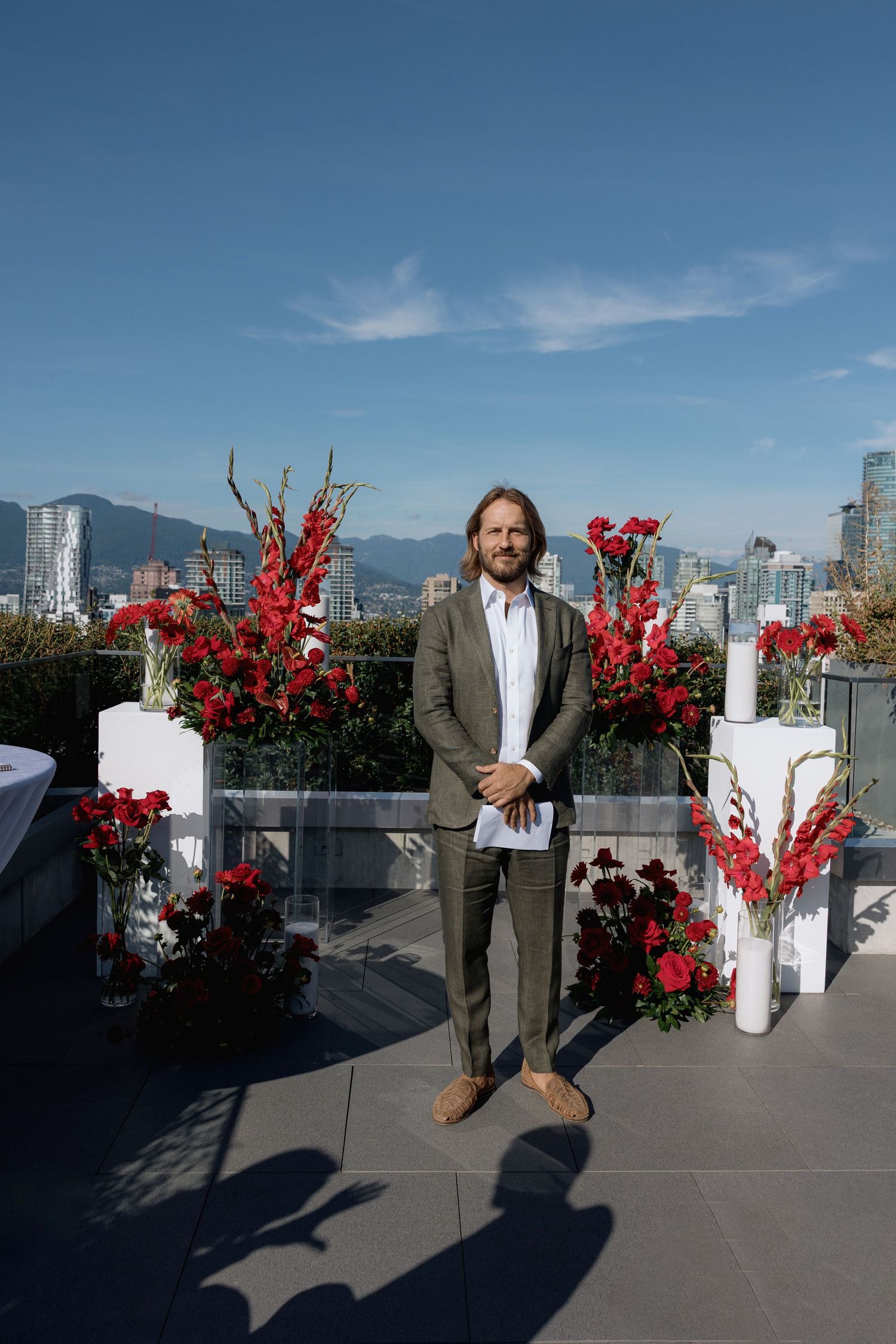 Rooftop event setup with white pedestals and bright red floral arrangements against a city skyline backdrop.